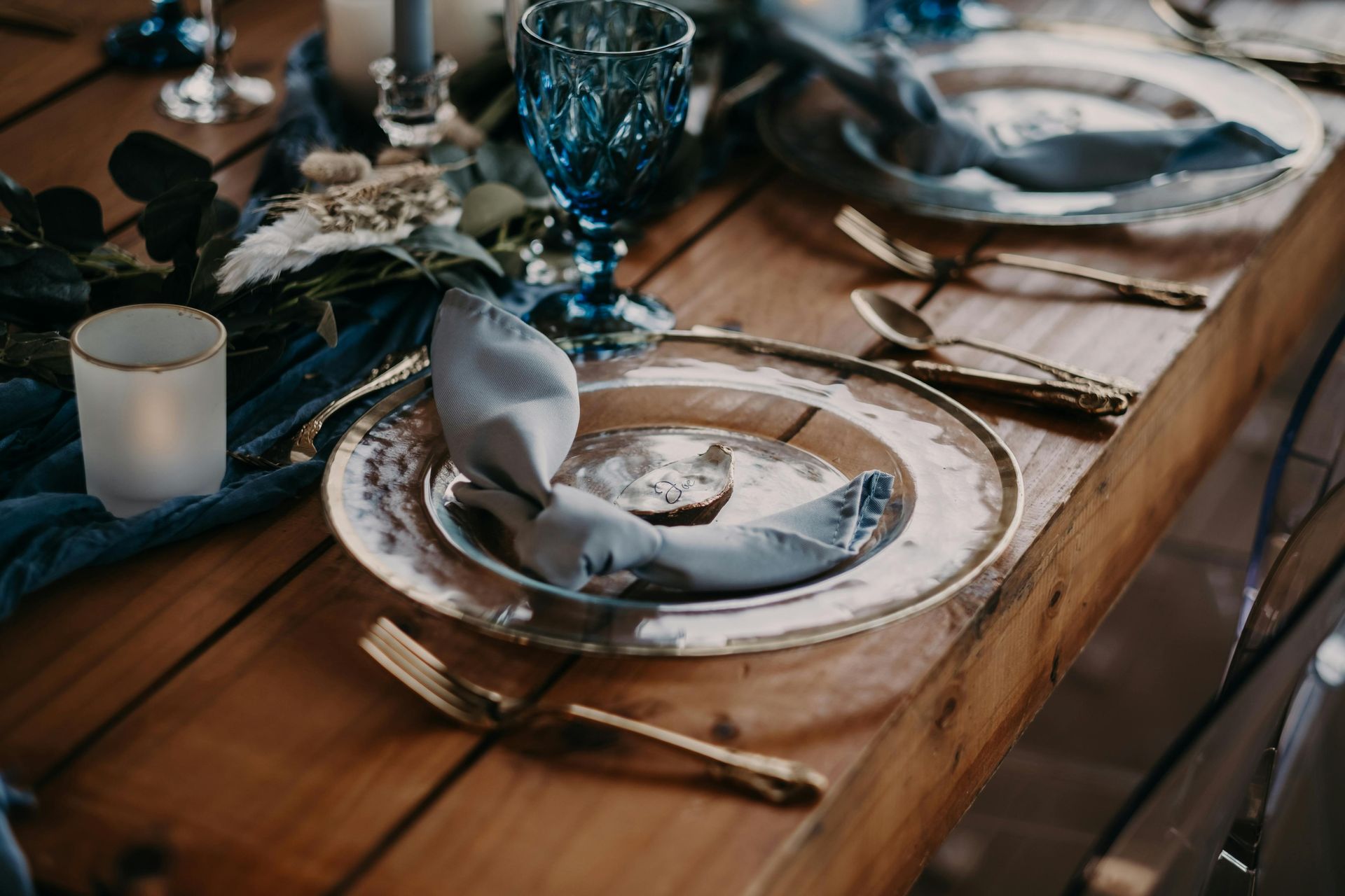 Rustic table setting with gold-rimmed plates, blue glassware, and folded napkin.