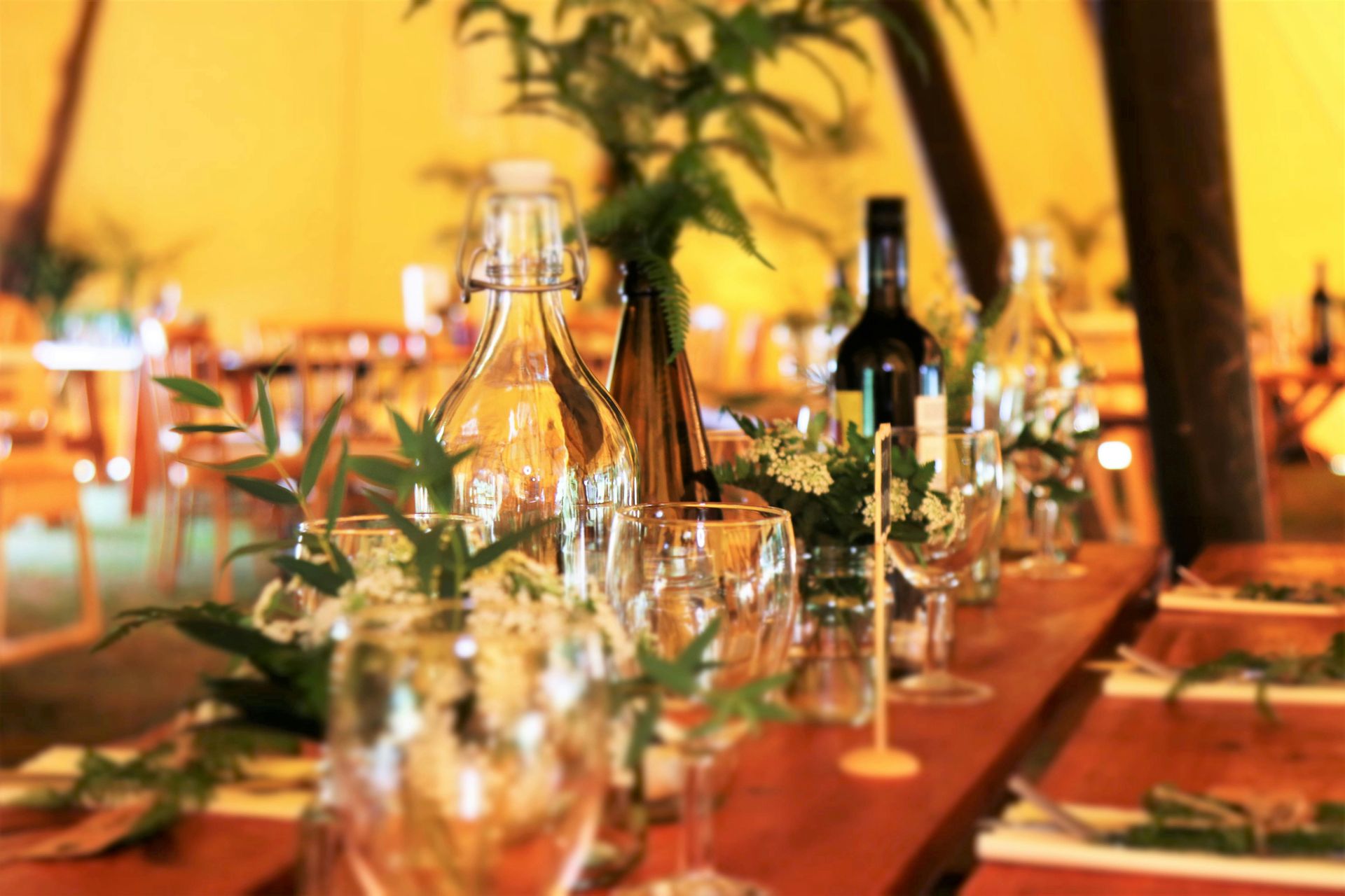 Wedding table setting with glassware, bottles, and floral arrangements.