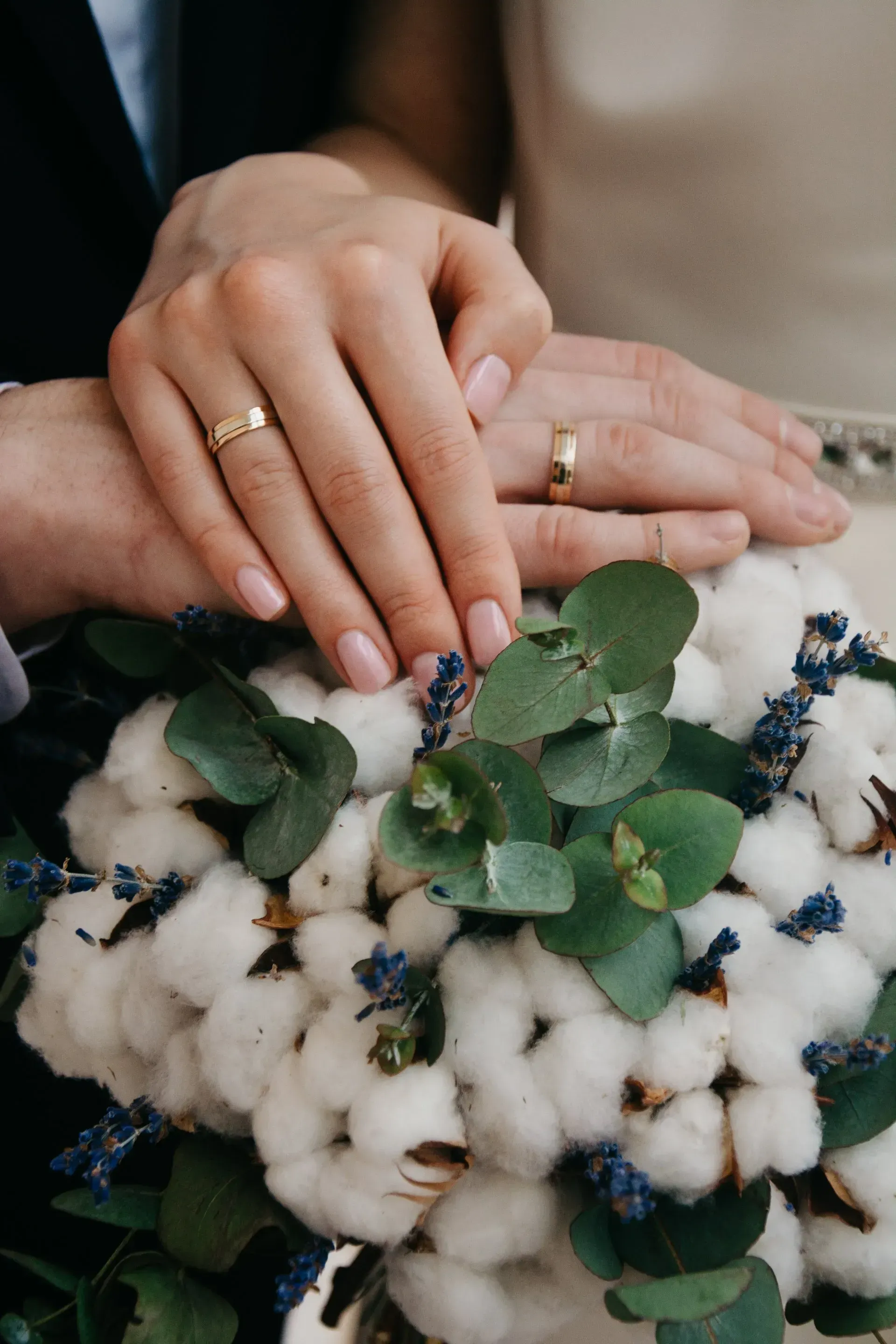 Hands with wedding rings resting on a cotton and eucalyptus bouquet. Hands with wedding rings resting on a cotton and eucalyptus bouquet.