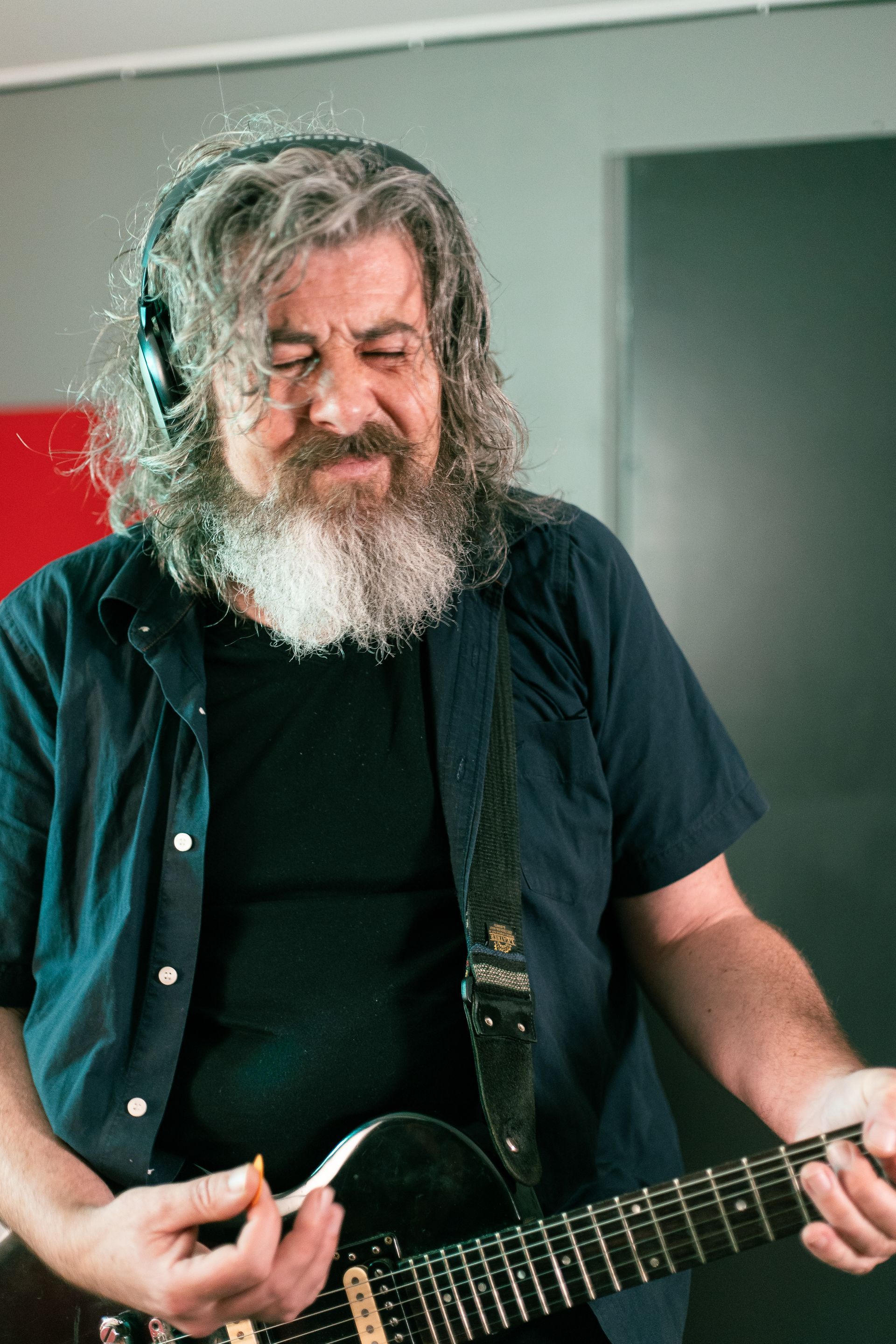 A man with a beard is playing a guitar and wearing headphones.