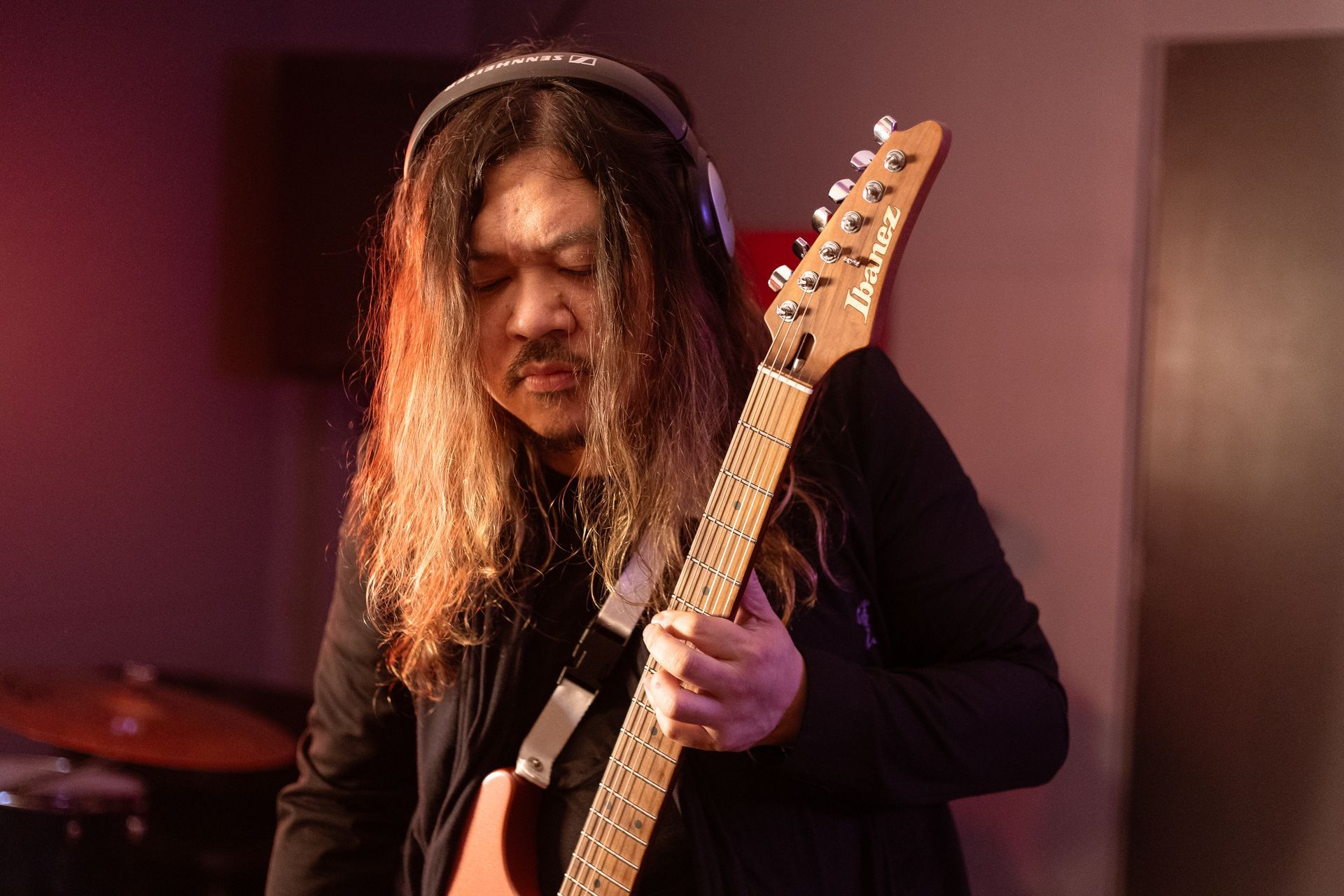 A man with long hair is playing an electric guitar while wearing headphones.