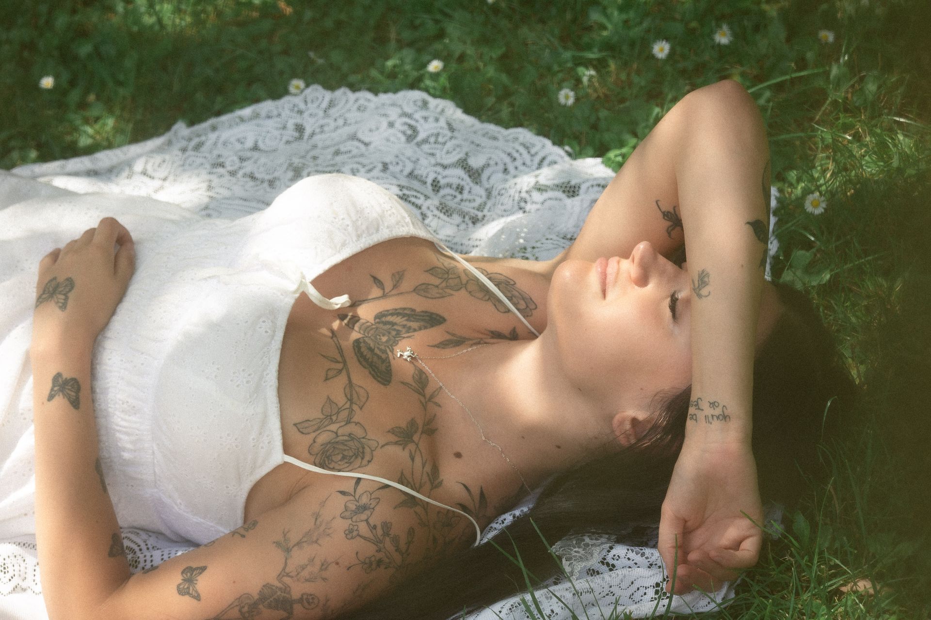 A woman with tattoos is laying on a blanket in the grass.