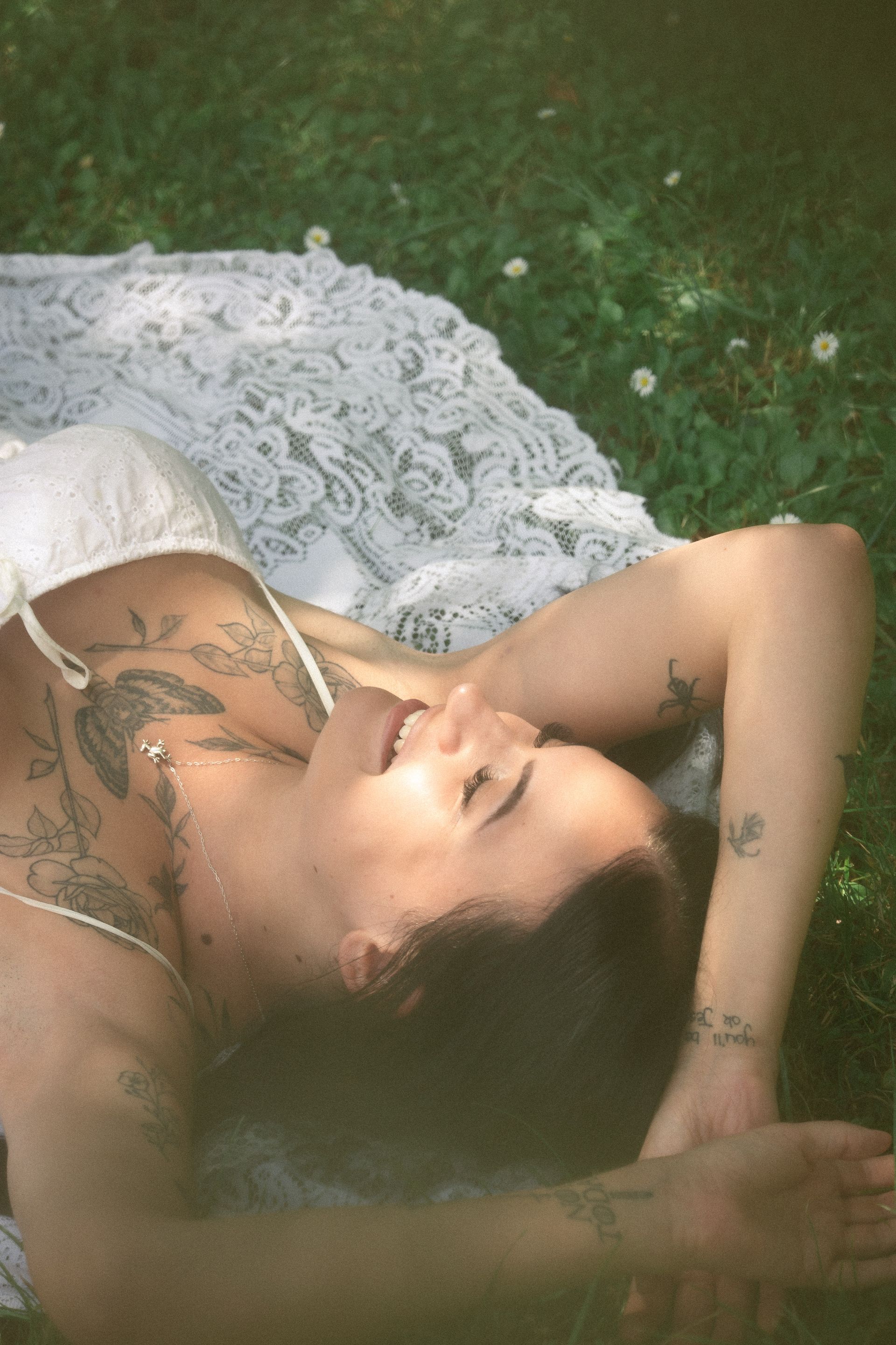A woman in a white dress is laying in the grass with her eyes closed.