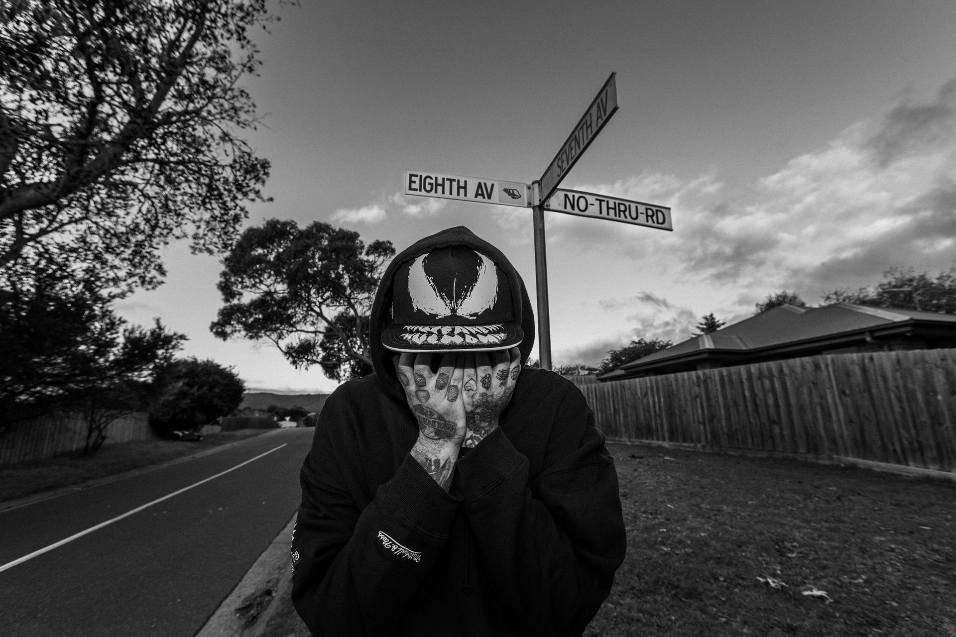 A man wearing a venom hat is standing in front of a street sign.