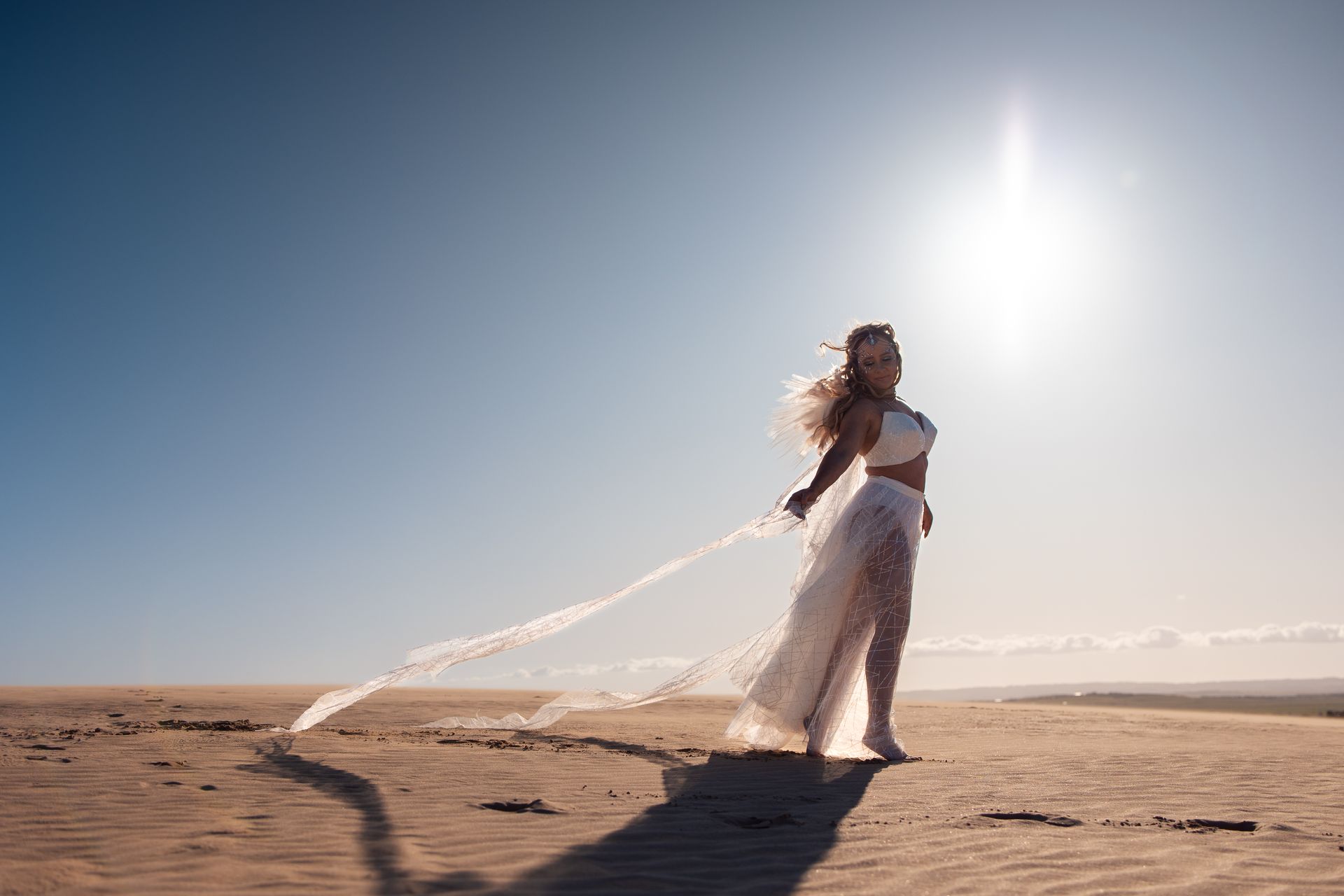 A woman in a white dress is standing on a sandy beach.