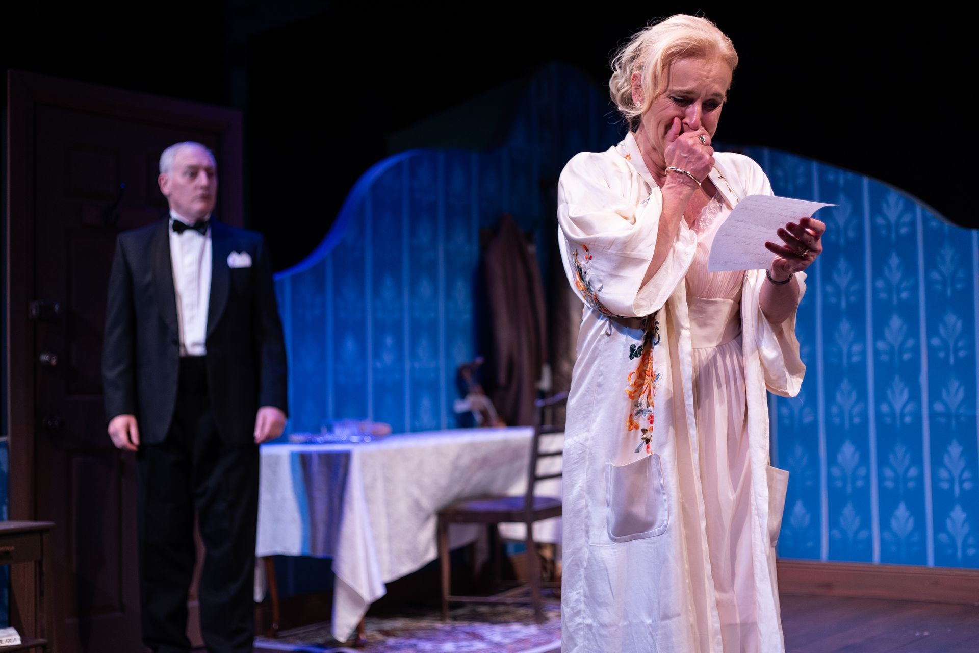 A man in a tuxedo is standing next to a woman in a white dress holding a piece of paper.