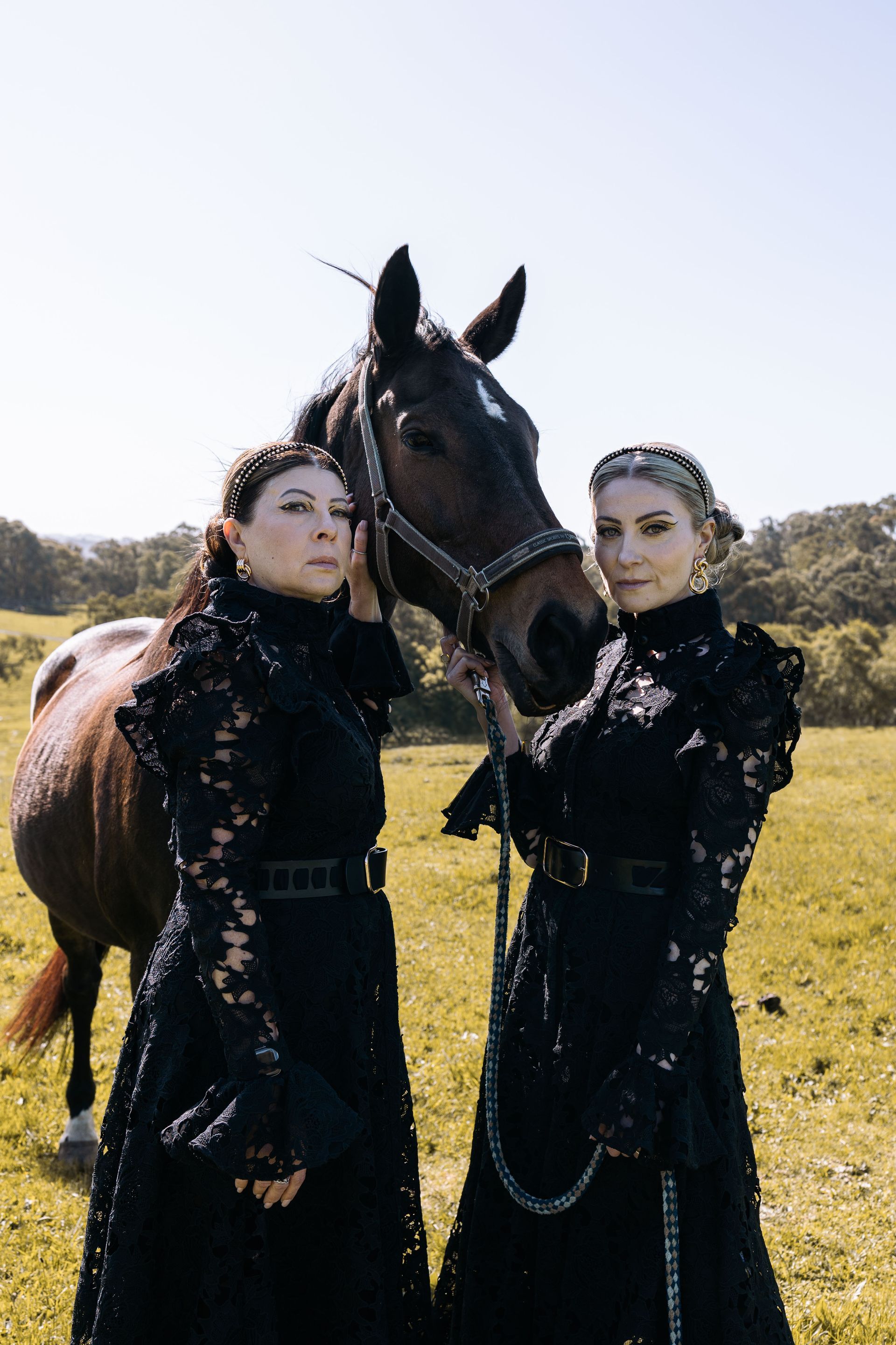 Two women in black dresses are standing next to a horse in a field.
