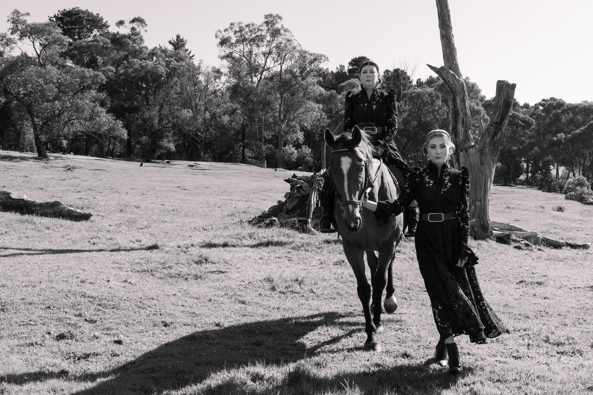 Two people riding horses in a field with trees in the background