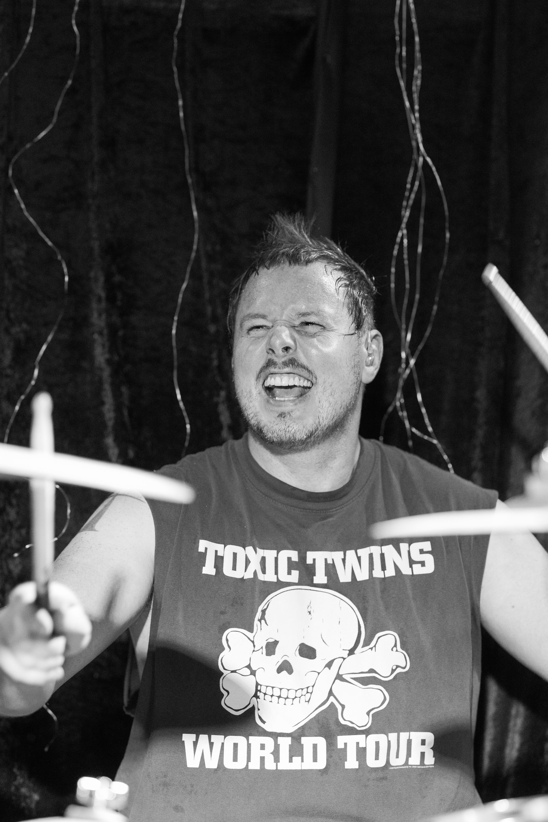 A man wearing a toxic twins world tour shirt is playing drums