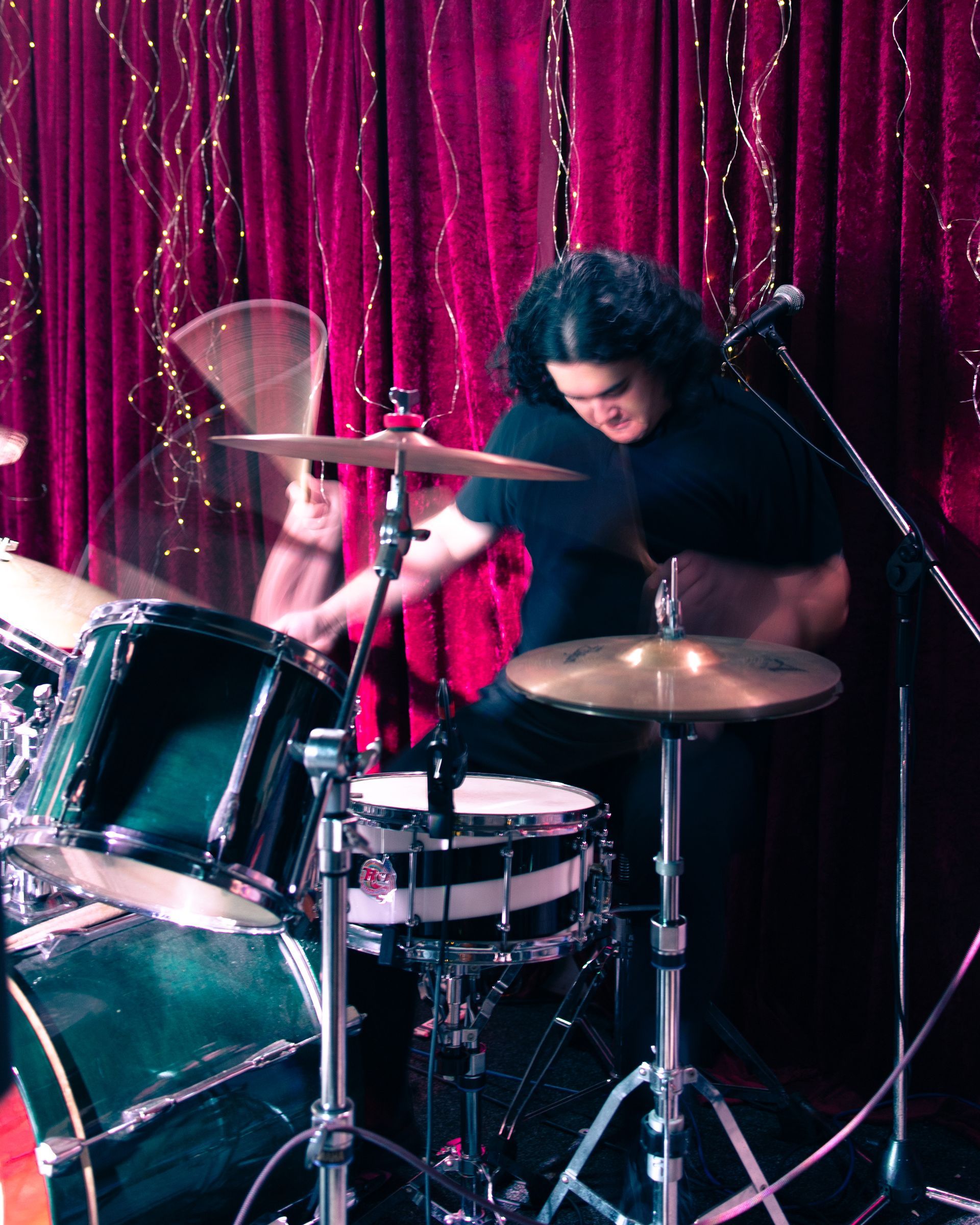 A man is playing drums in front of a red curtain
