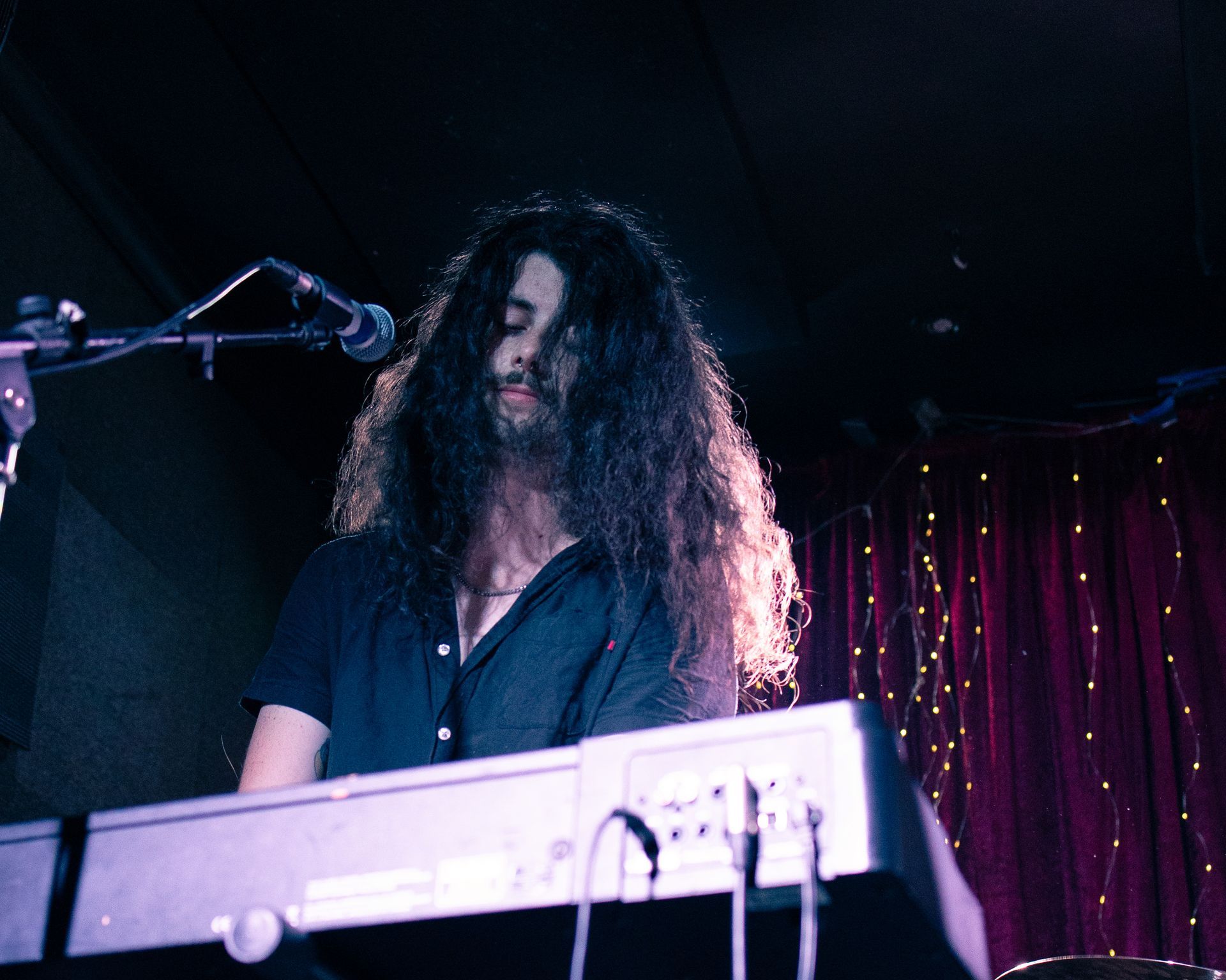 A man with long hair is playing a keyboard in front of a microphone