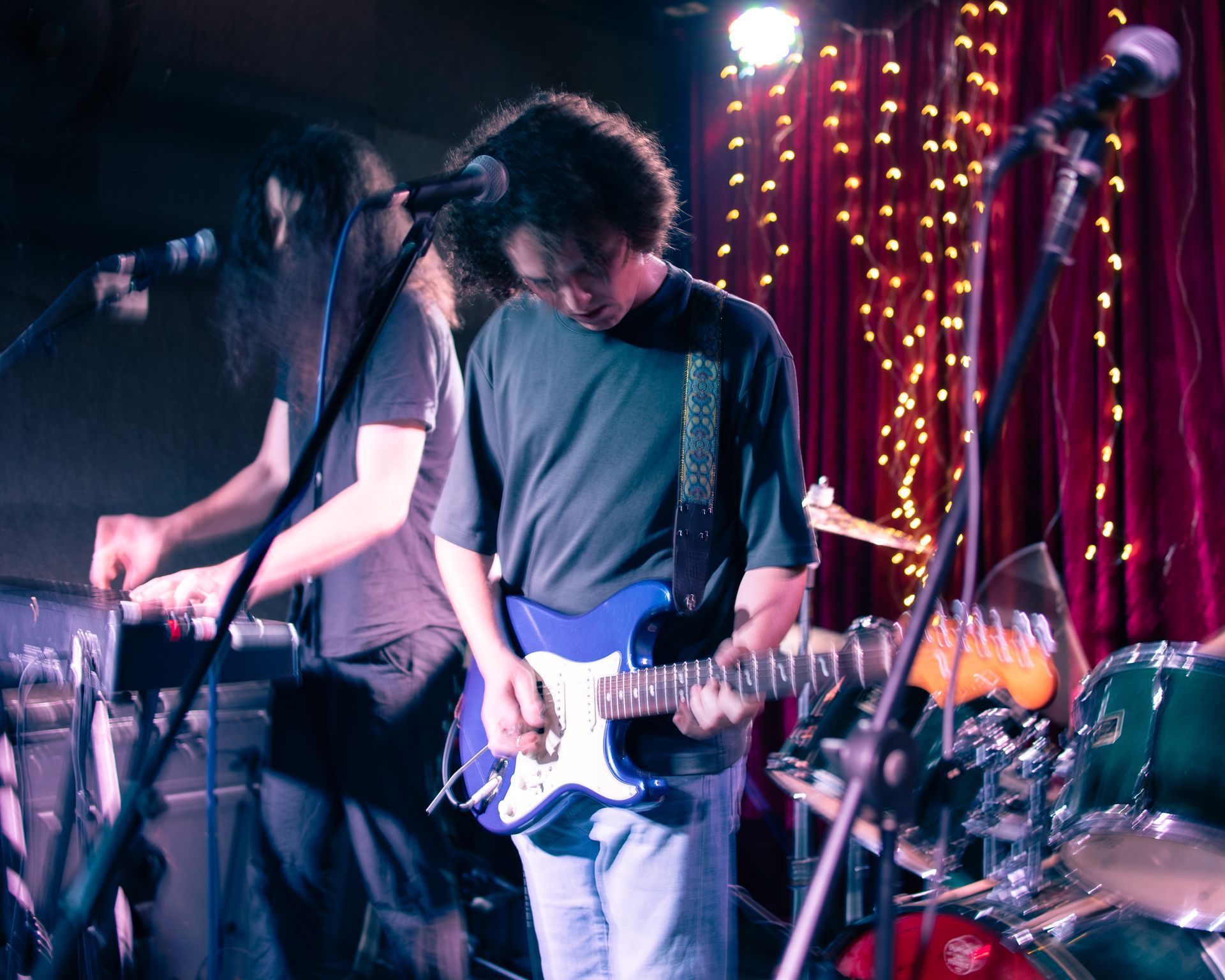 A man playing a guitar in front of a red curtain