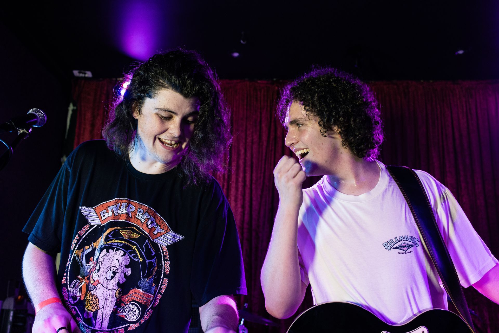 Two men are standing next to each other on a stage playing guitars and singing into microphones.