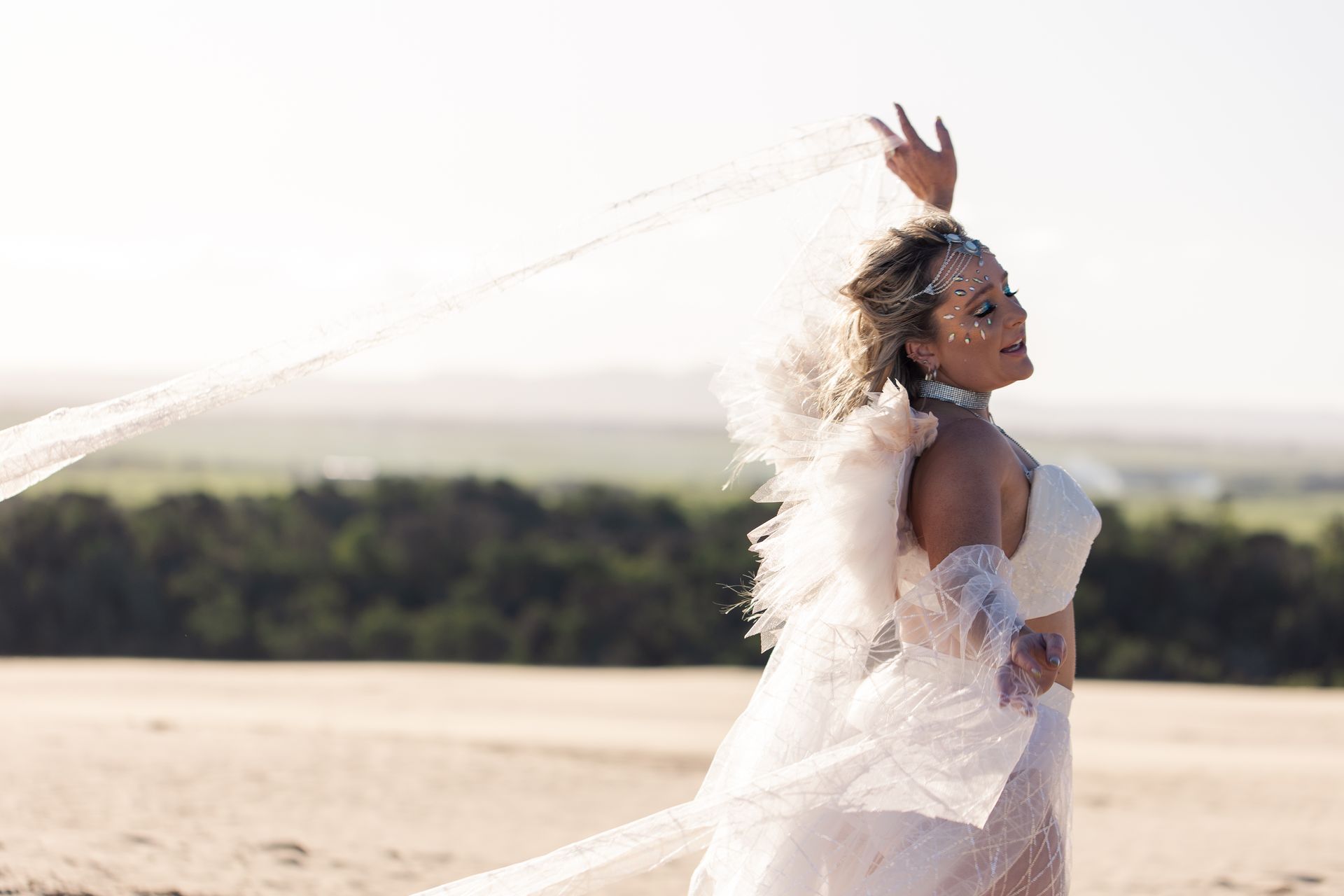 A woman in a white dress and veil is standing in the sand.
