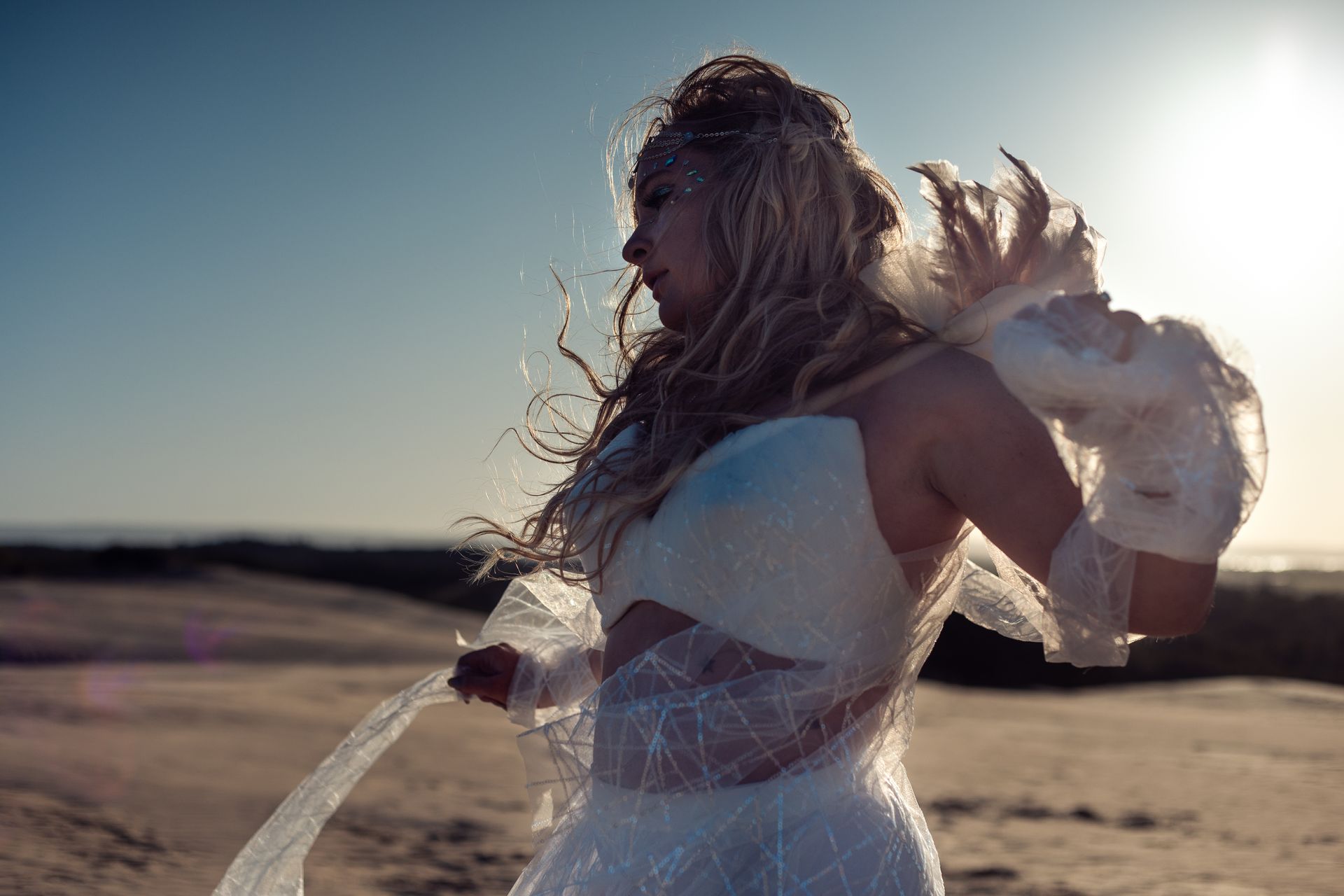 A woman in a white dress is standing in the sand.