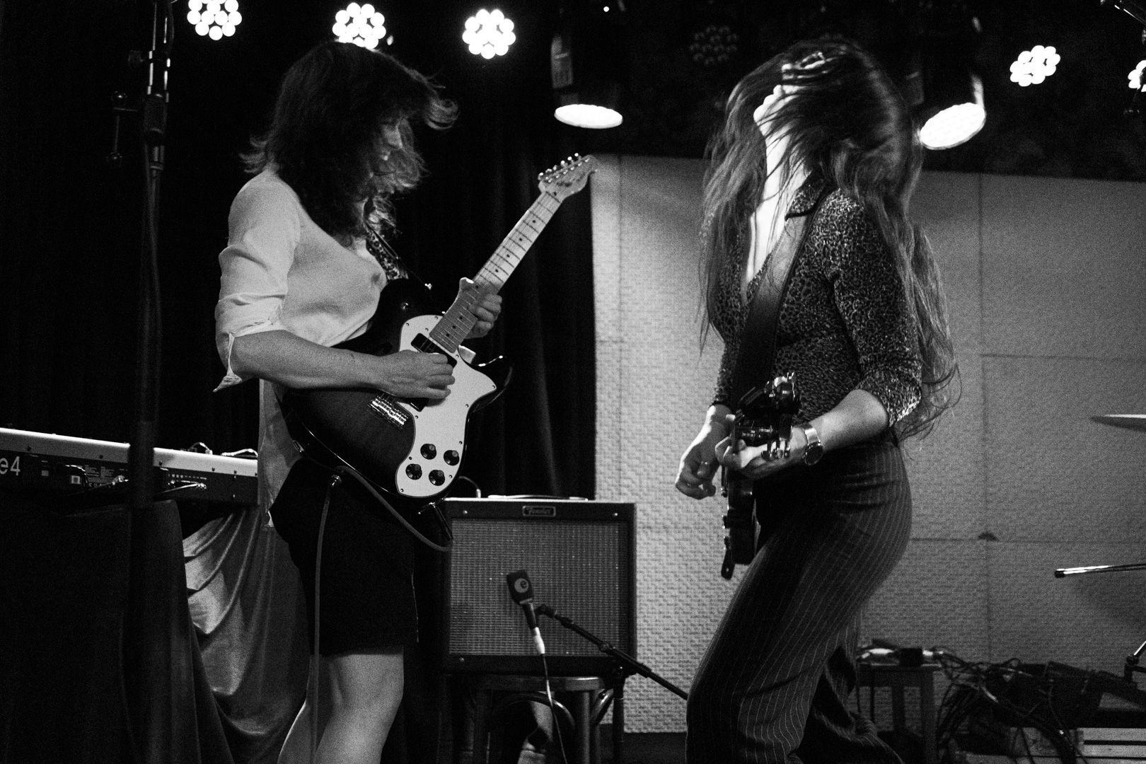 Two women are playing guitars on a stage in a black and white photo.