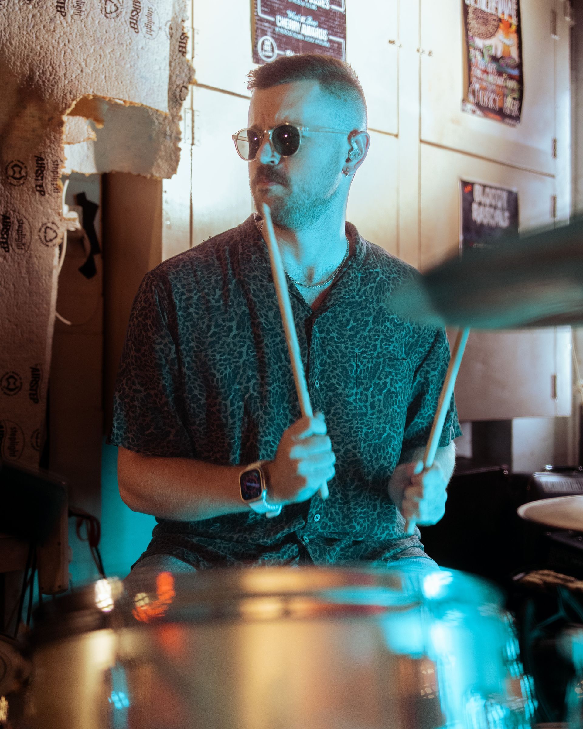 A man wearing sunglasses is playing drums in a room.