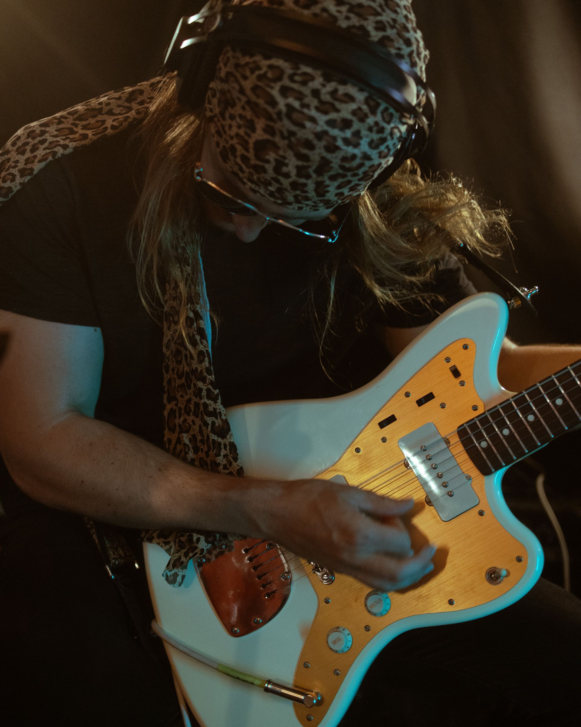 A man wearing a leopard print scarf is playing a guitar