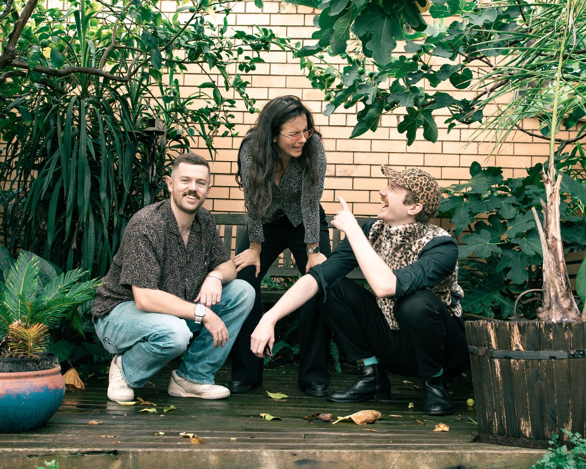 A group of people are sitting on a wooden deck in front of a brick wall.
