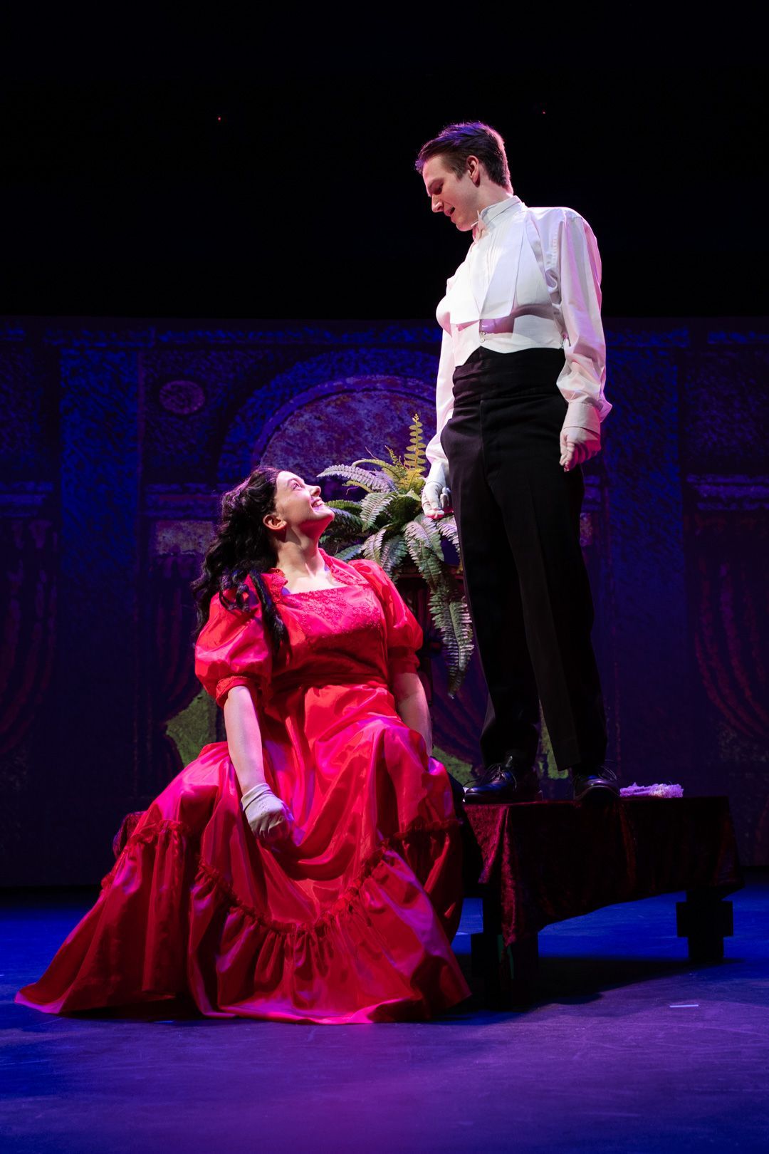 A man and a woman are standing next to each other on a stage . the woman is wearing a red dress.
