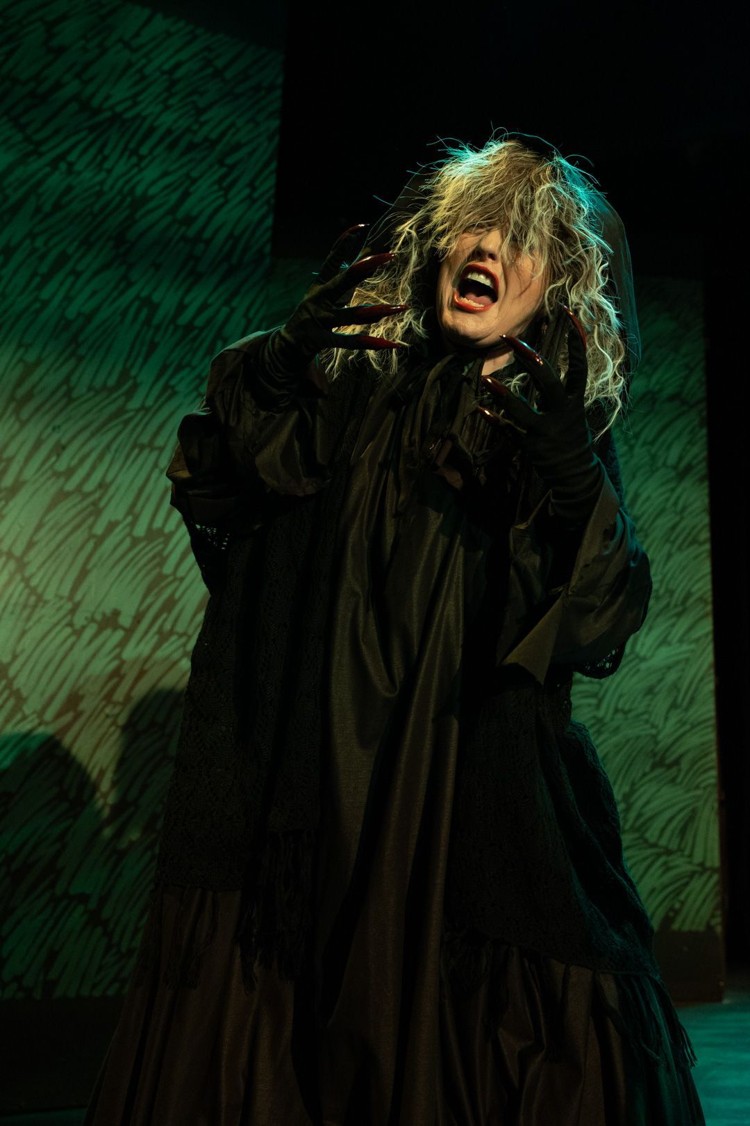 A woman in a black dress and veil is screaming on a stage.