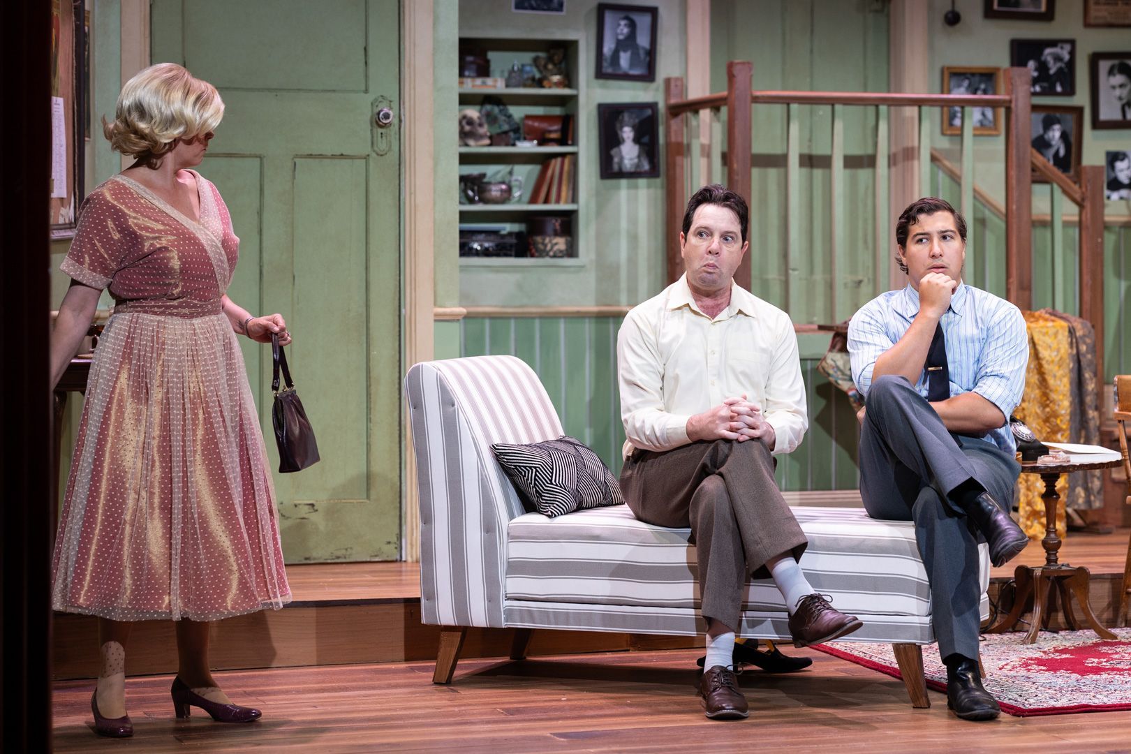 A woman is standing next to two men sitting on a couch in a living room.