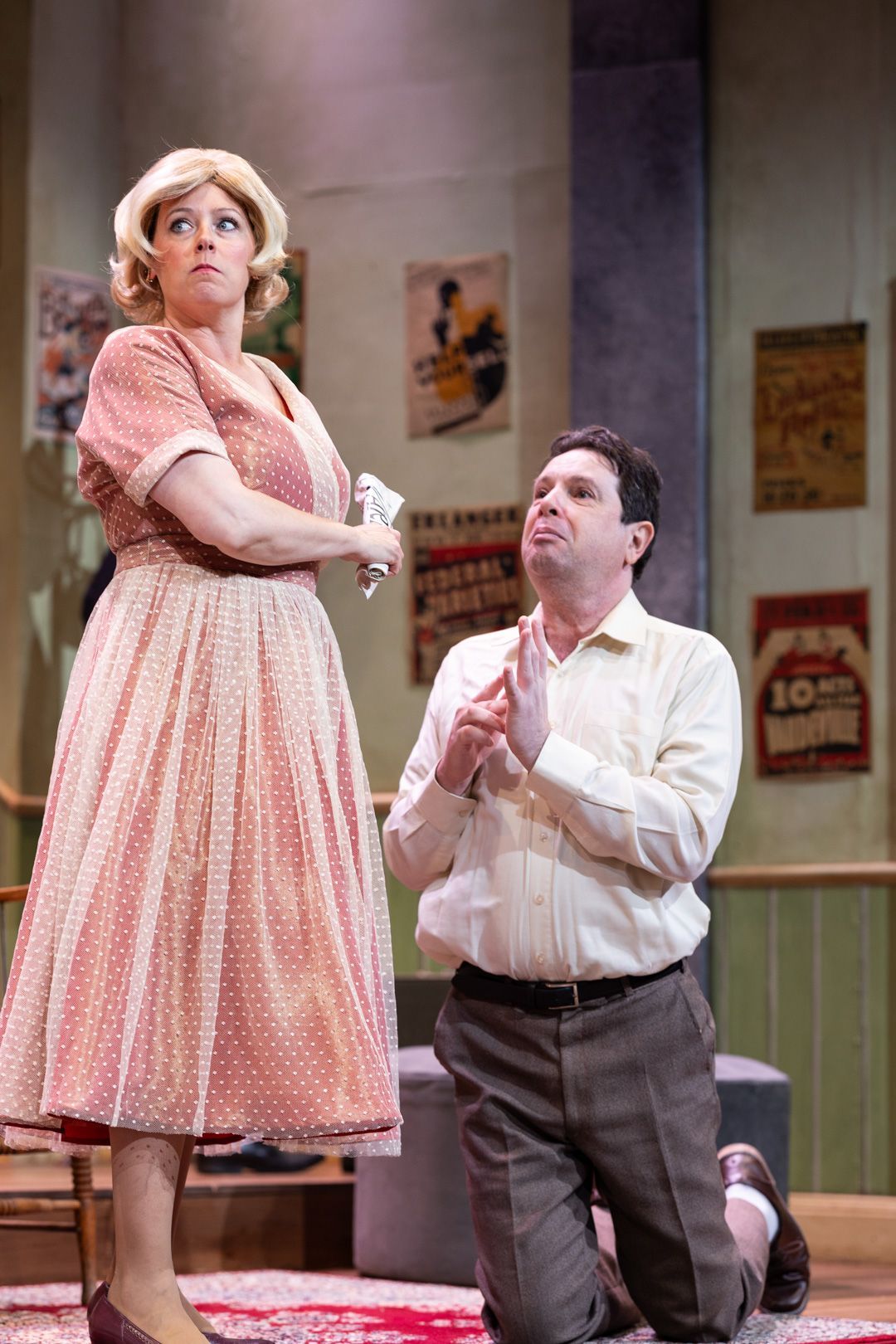A man is kneeling down next to a woman on a stage in a play.