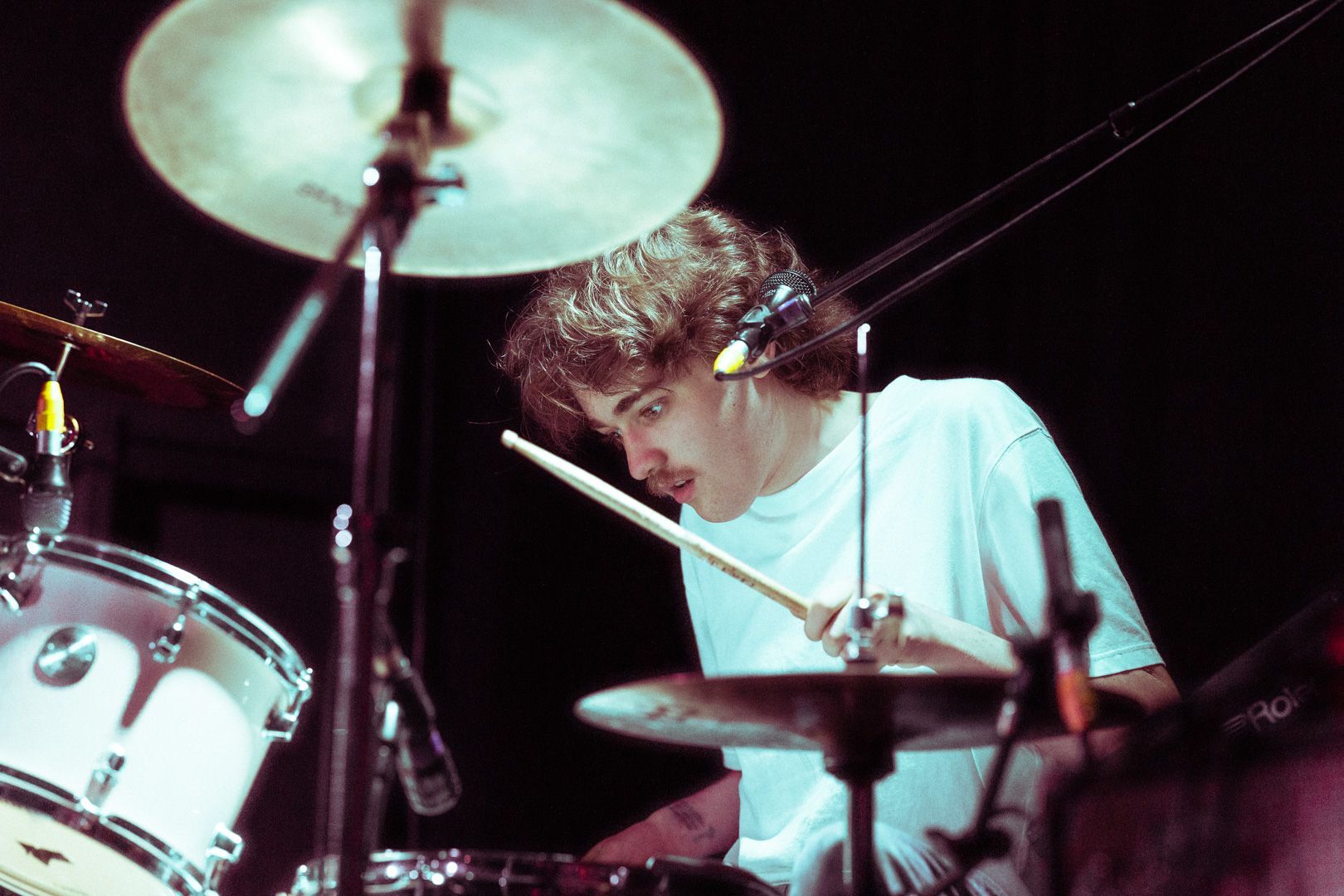A man in a white shirt is playing drums on a stage.