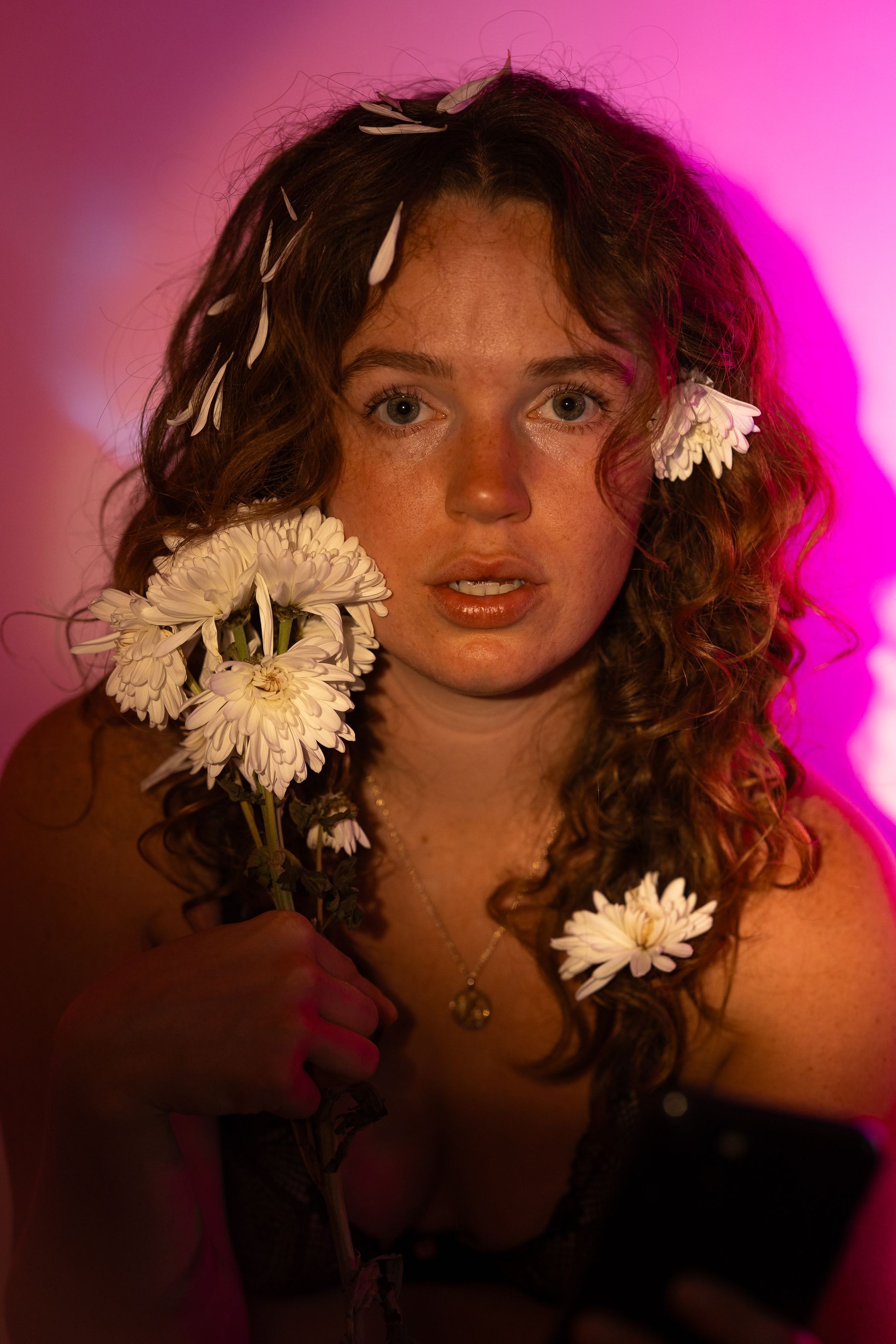 A woman with curly hair is holding a bunch of flowers in her hair.