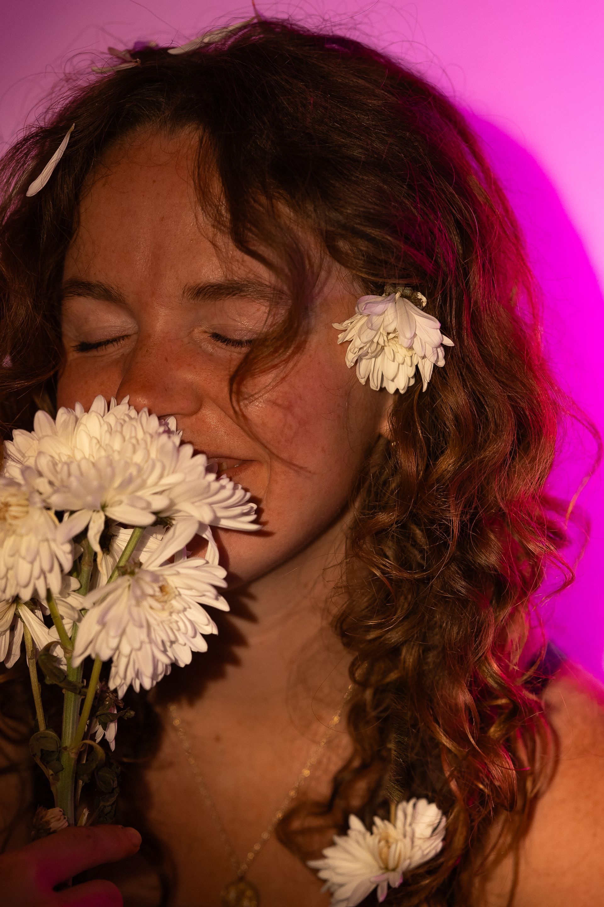 A woman with curly hair is smelling a bouquet of white flowers.