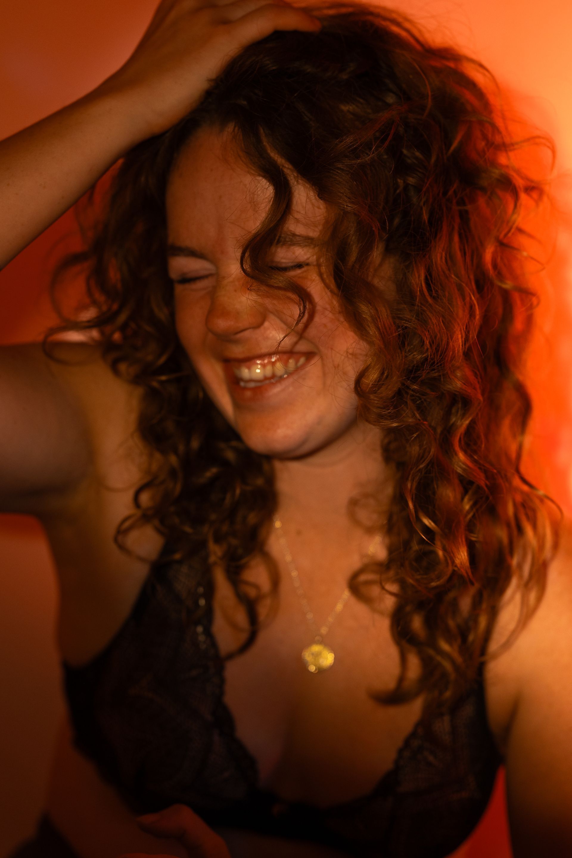 A woman with curly hair is wearing a black bra and smiling.