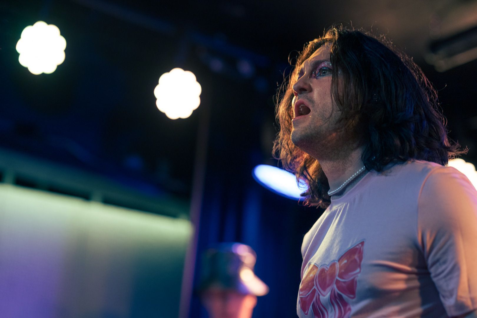 A man with long hair is singing into a microphone on a stage.