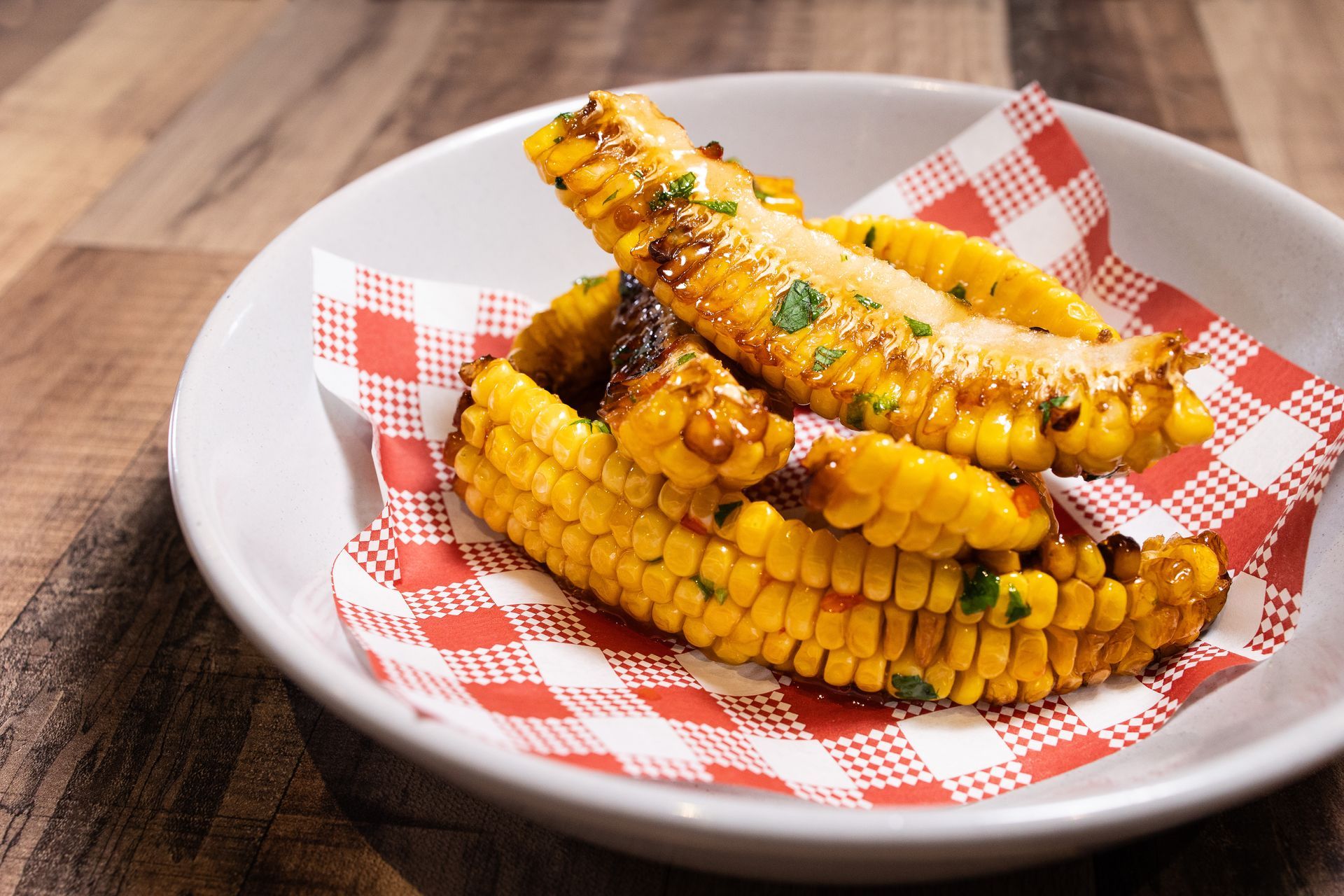 A white plate topped with corn on the cob on a checkered napkin.