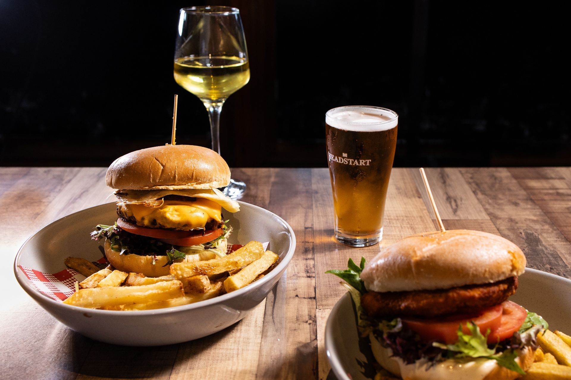 Two hamburgers , french fries , and a glass of beer are on a wooden table.
