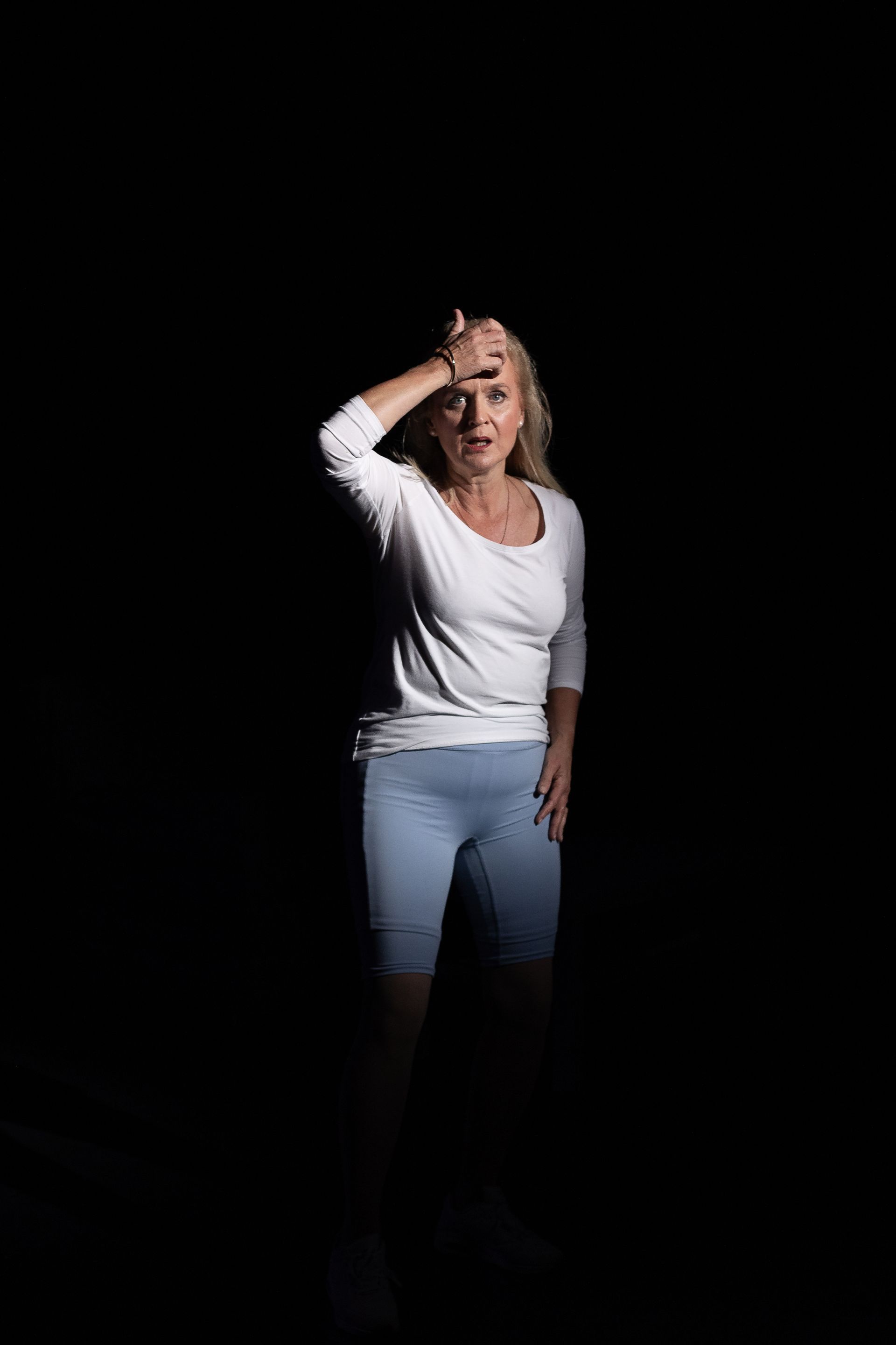 A woman in a white shirt and blue shorts is standing in the dark.