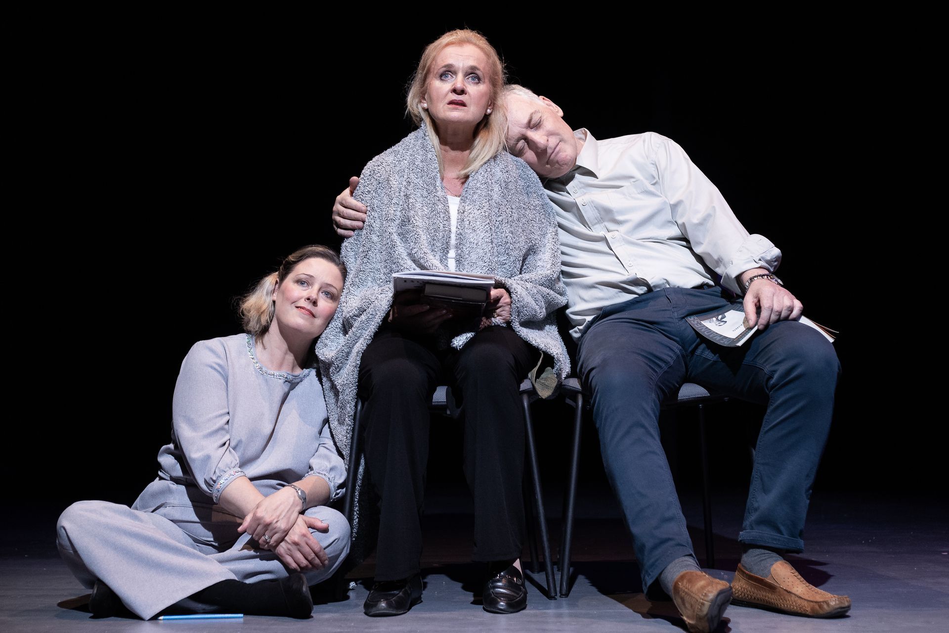 A man and two women are sitting on a couch on a stage.