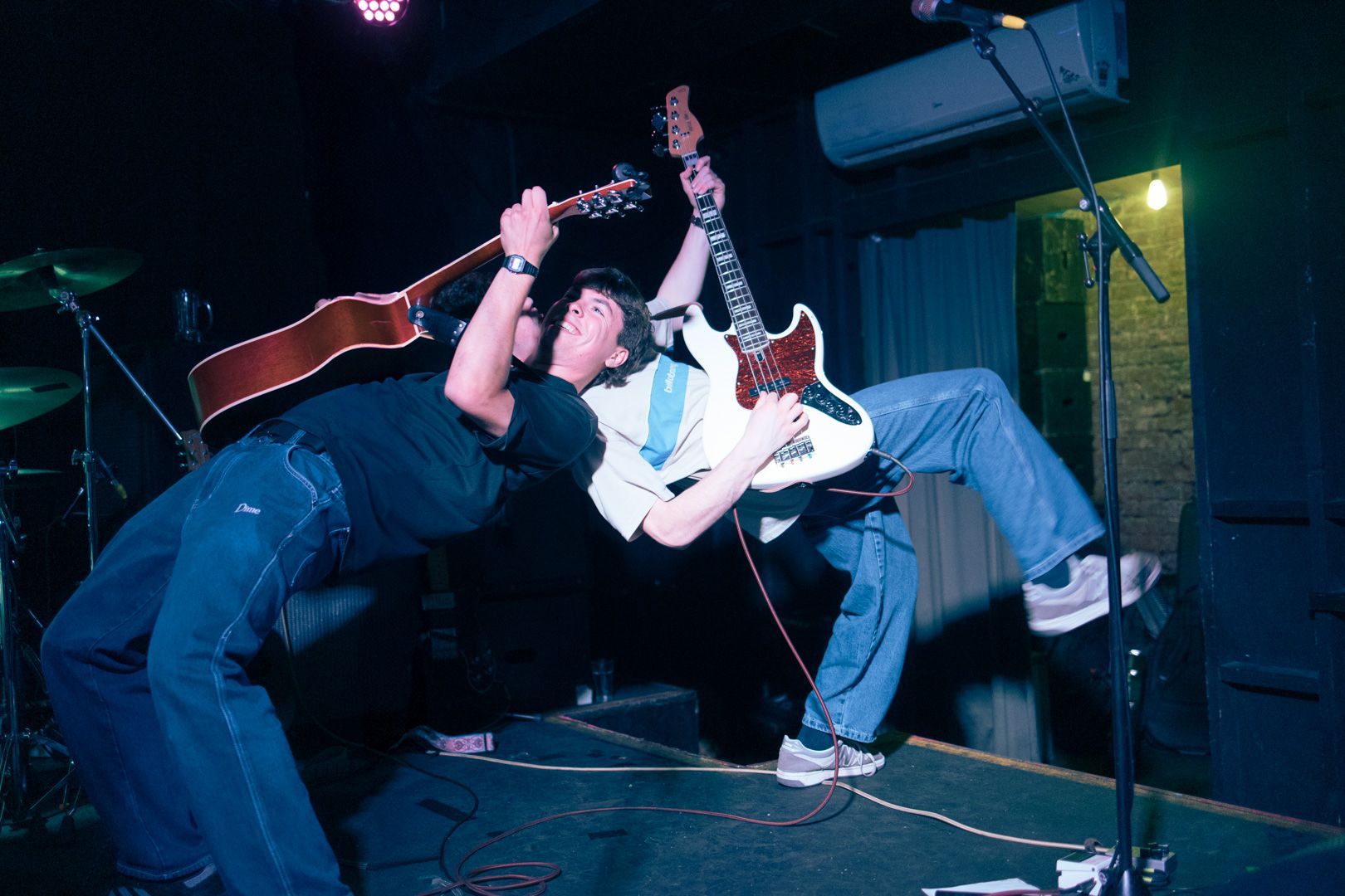 Two men are playing guitars on a stage in a dark room