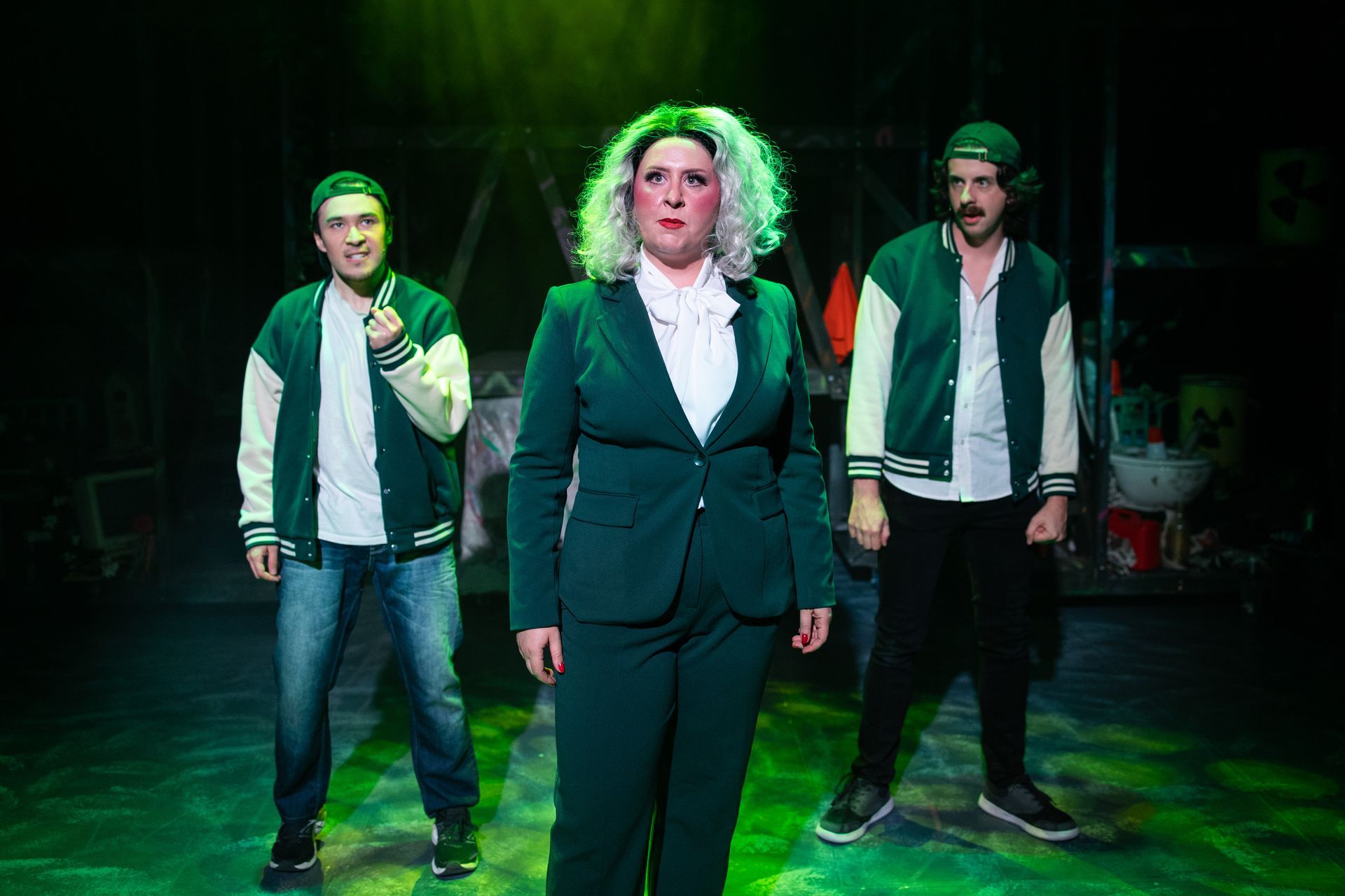 A woman in a green suit is standing next to two men on a stage.