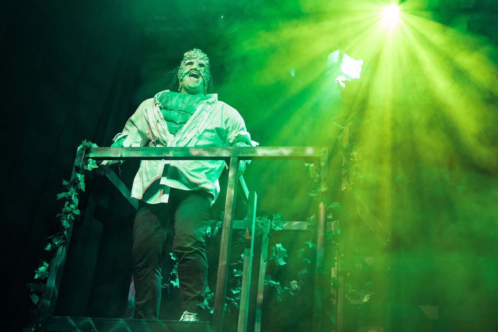 A man in a mummy costume is standing on a stage in front of a green light.