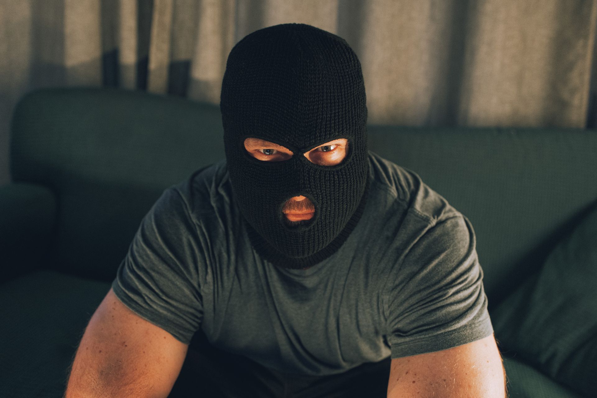 A man wearing a ski mask is sitting on a couch.