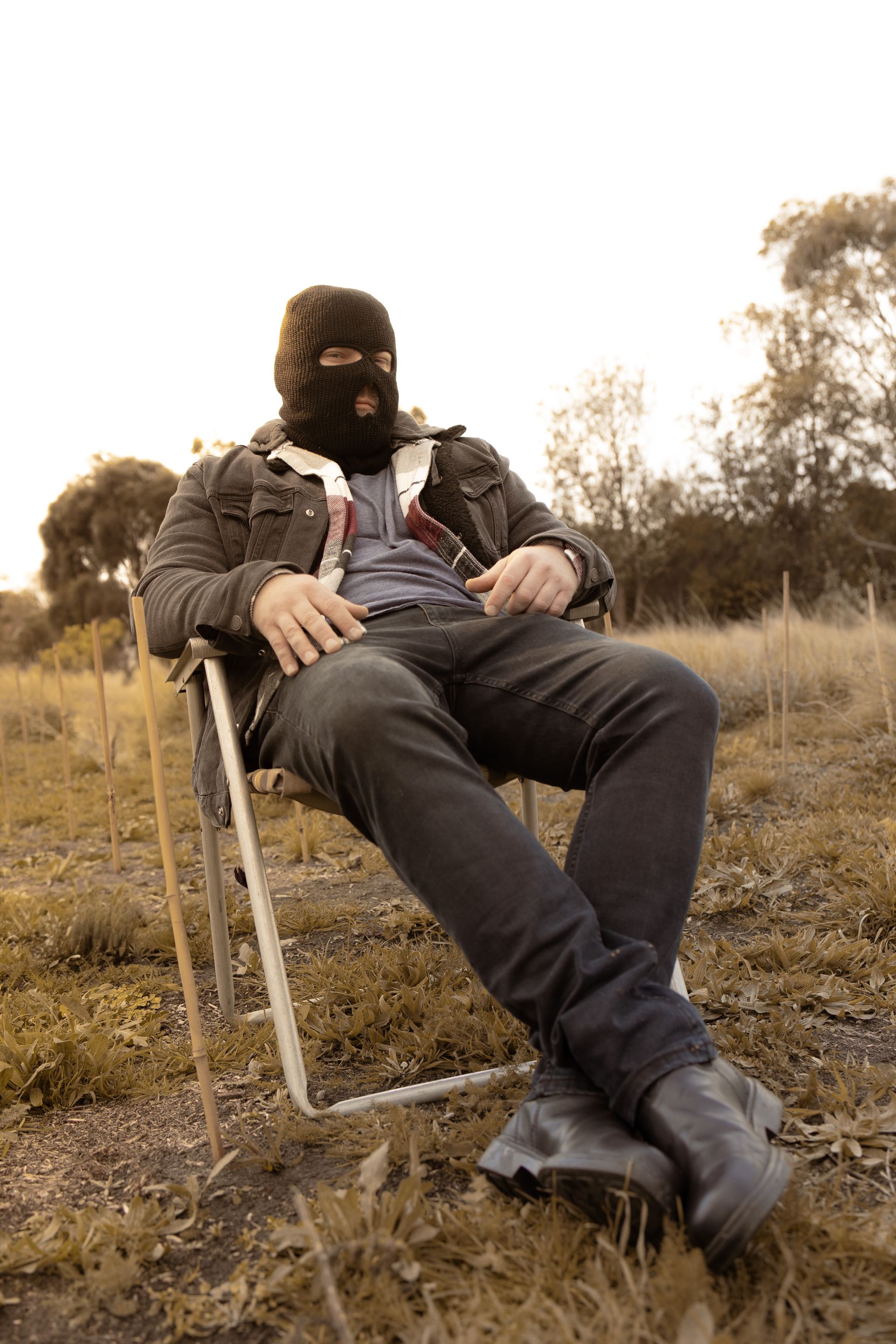 A man wearing a ski mask is sitting in a chair in a field.