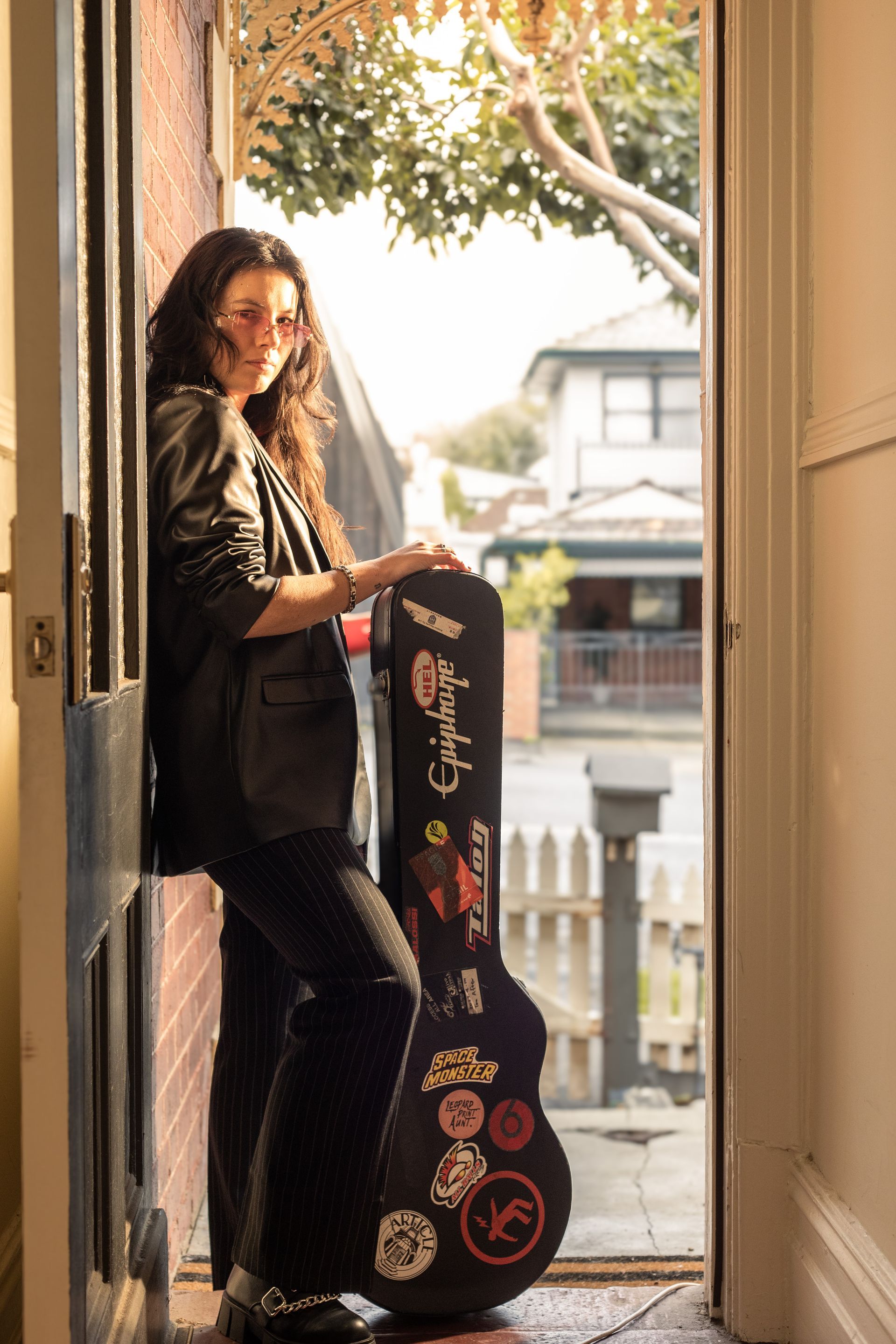 A woman is leaning against a door holding a guitar case.