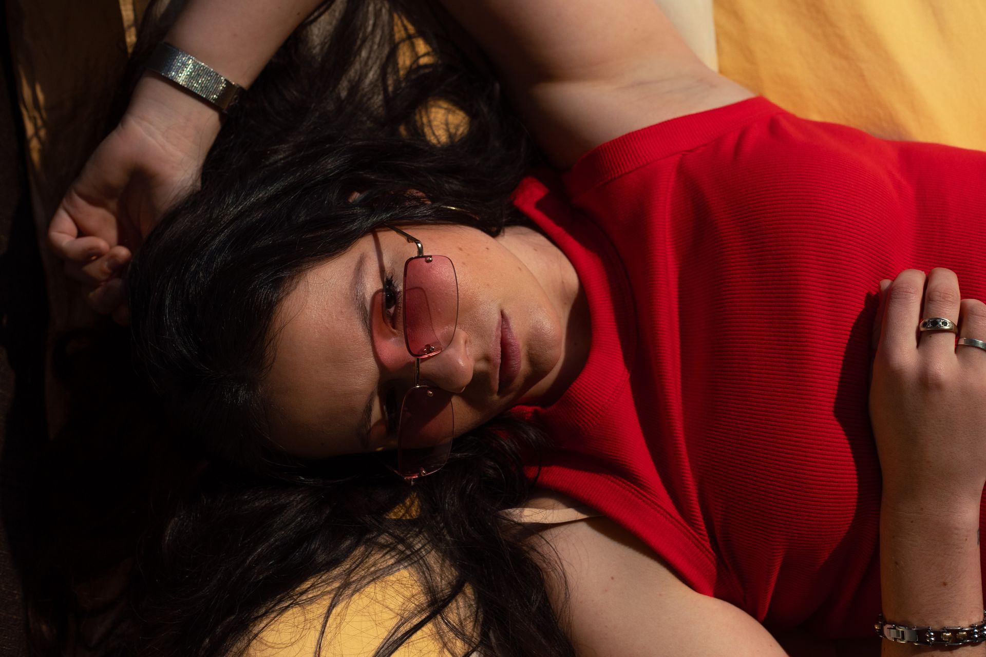 A woman in a red shirt and sunglasses is laying on the floor.