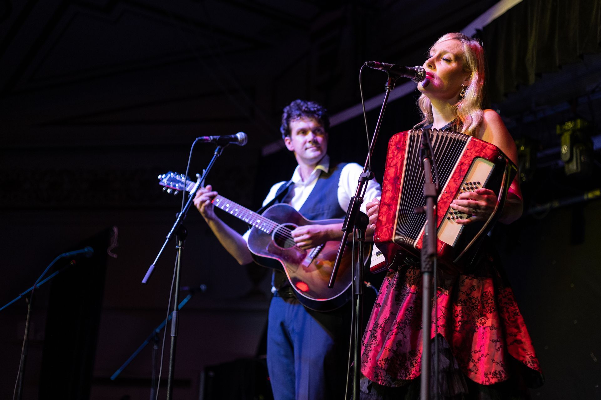 A man is playing a guitar and a woman is playing an accordion on stage.