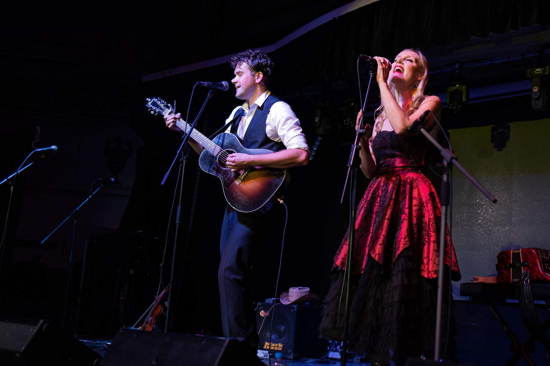 A man is playing a guitar and a woman is singing into a microphone on a stage.