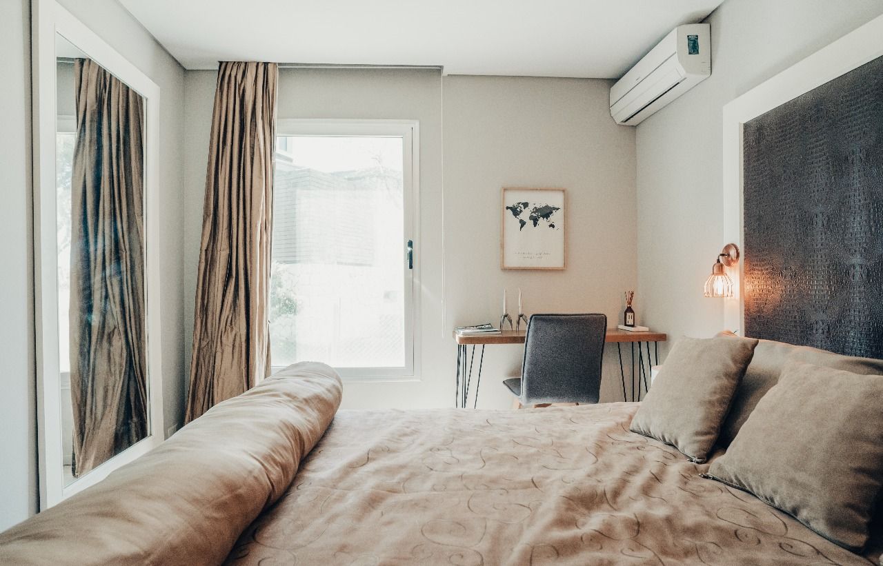Un dormitorio con cama, escritorio, espejo y ventana.