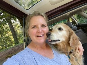 A woman is sitting in the back seat of a car holding a dog. About-Rosemary Michaels LMP