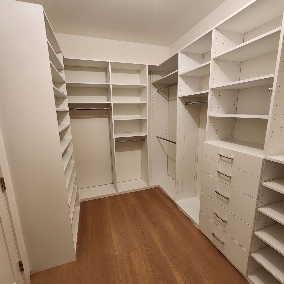 White closet organization system with shelves, drawers, and hanging rods. Wooden floor.