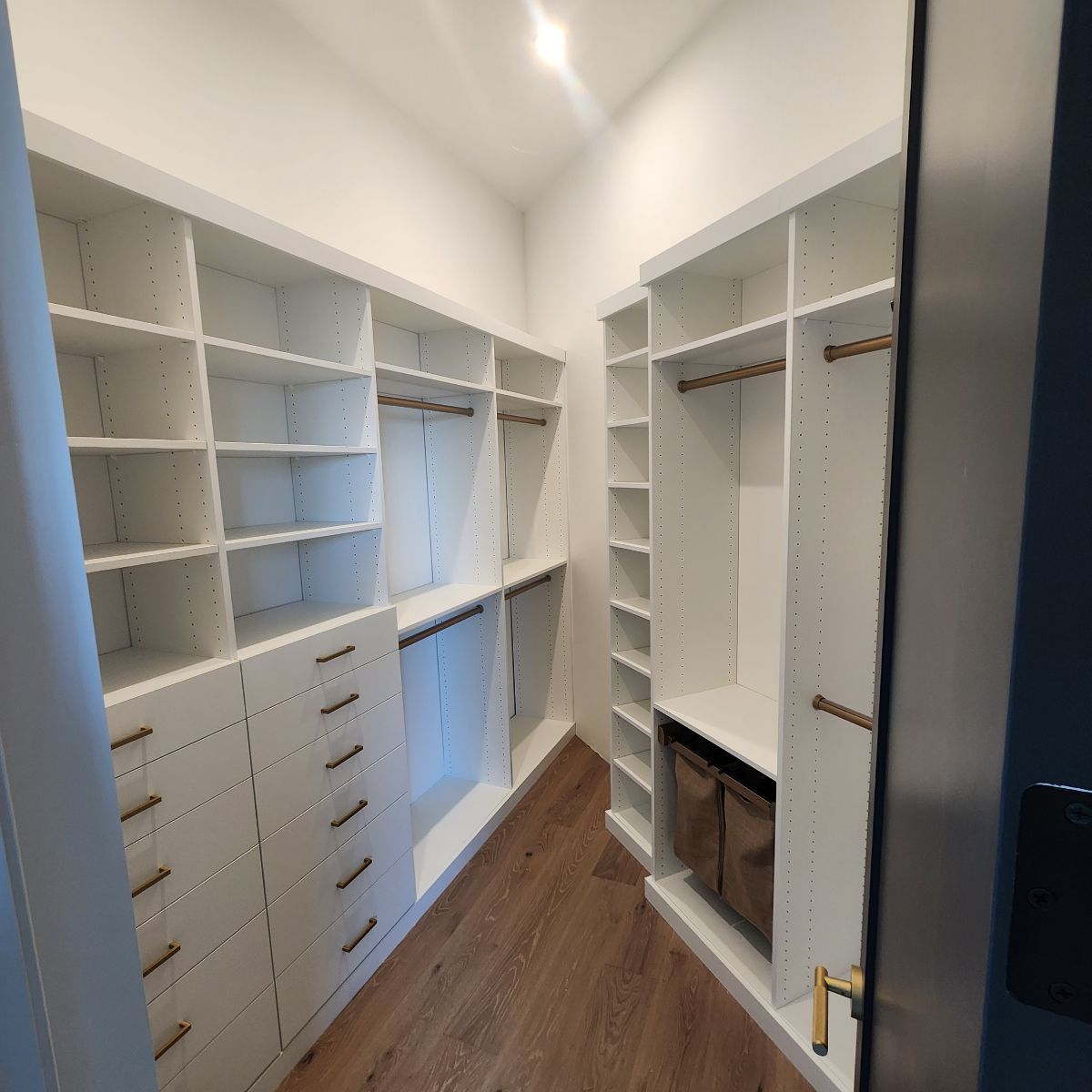 White walk-in closet with shelves, drawers, and hanging rods. Brown wood-look floor. Golden hardware.