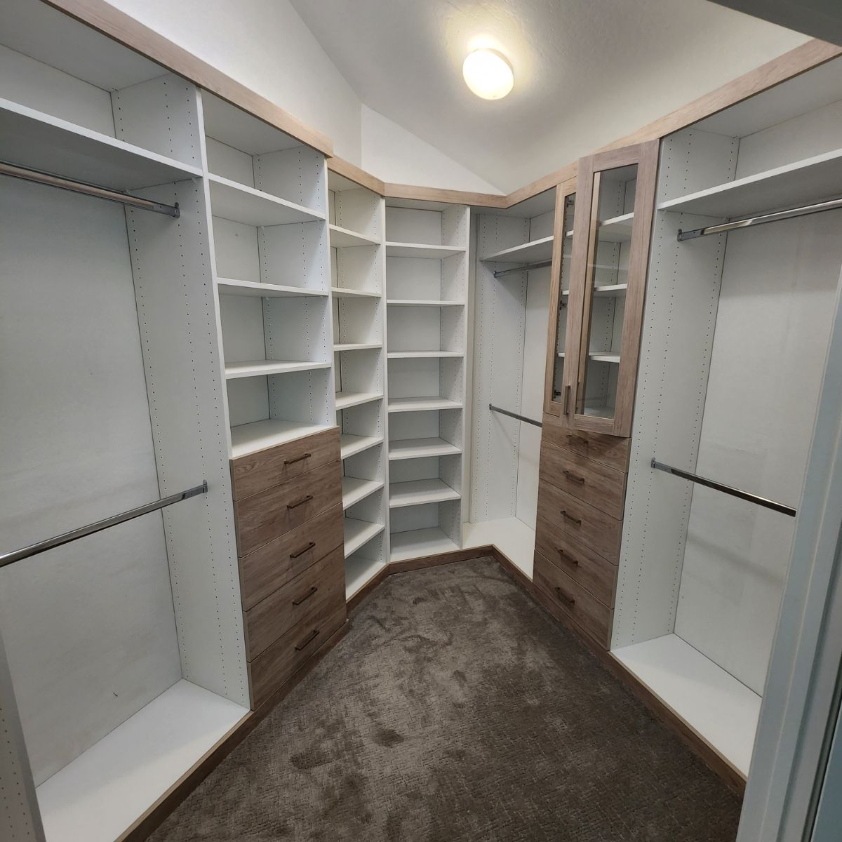 Walk-in closet with beige and white shelving, brown drawers, and clothes rods on a brown carpet.